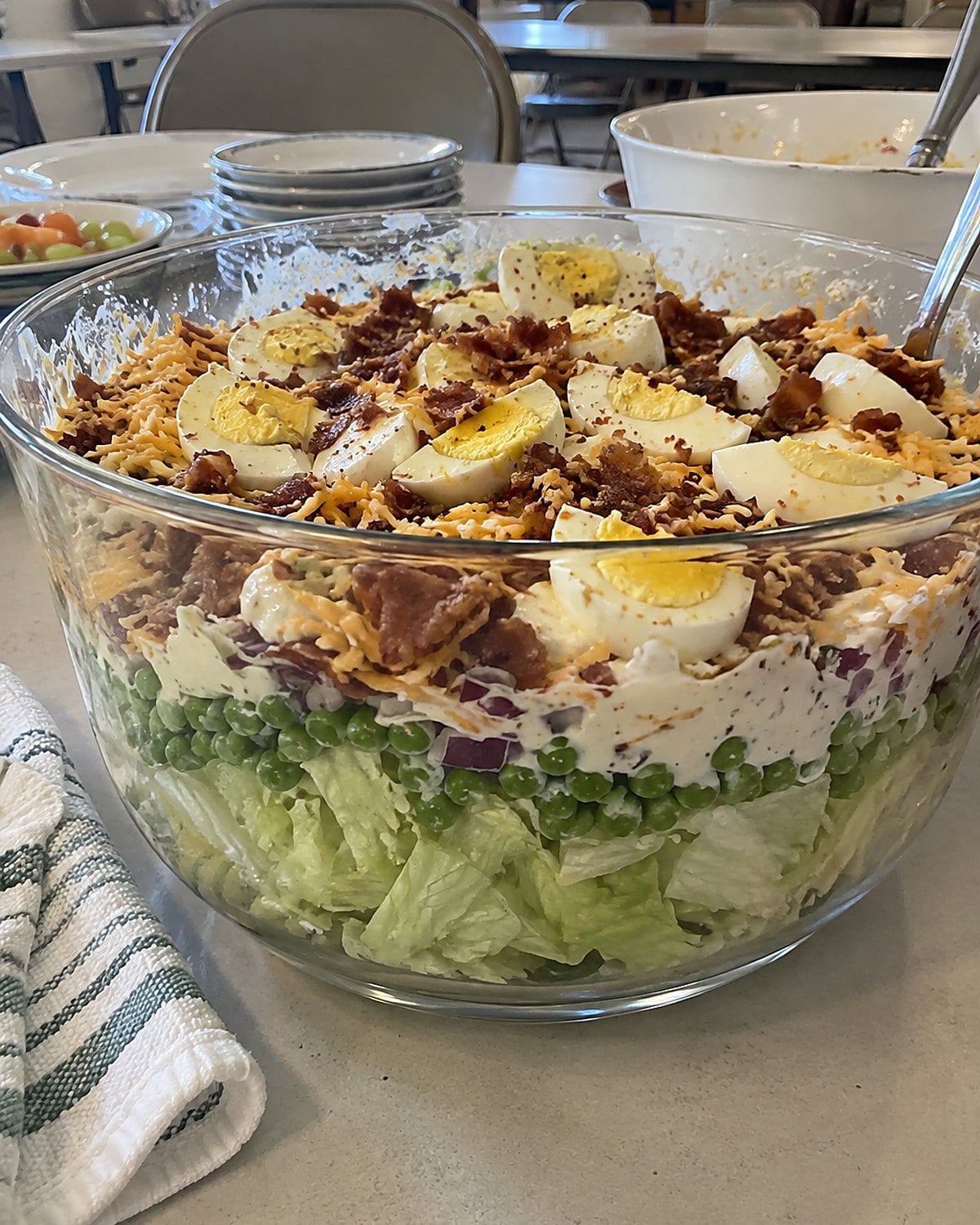 A clear bowl of layered salad on a church hall table, with peas and lettuce visible through the glass.
