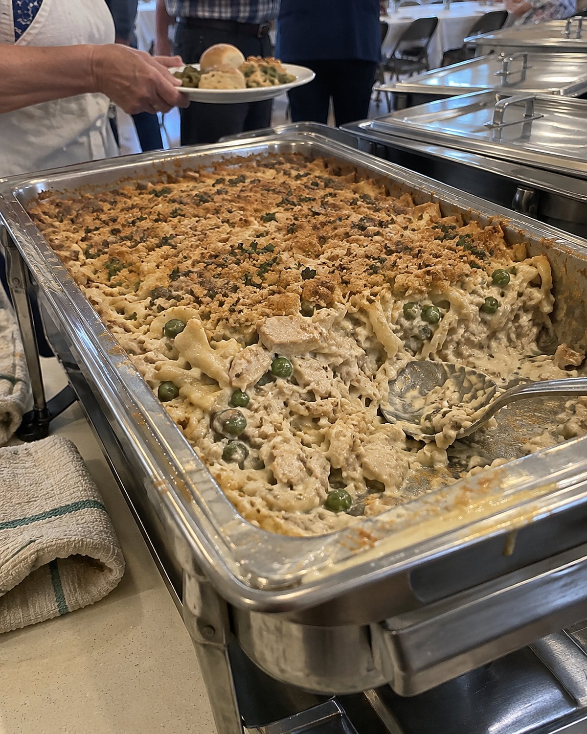 A steam table pan of chicken tetrazzini at the end of a church hall serving line.