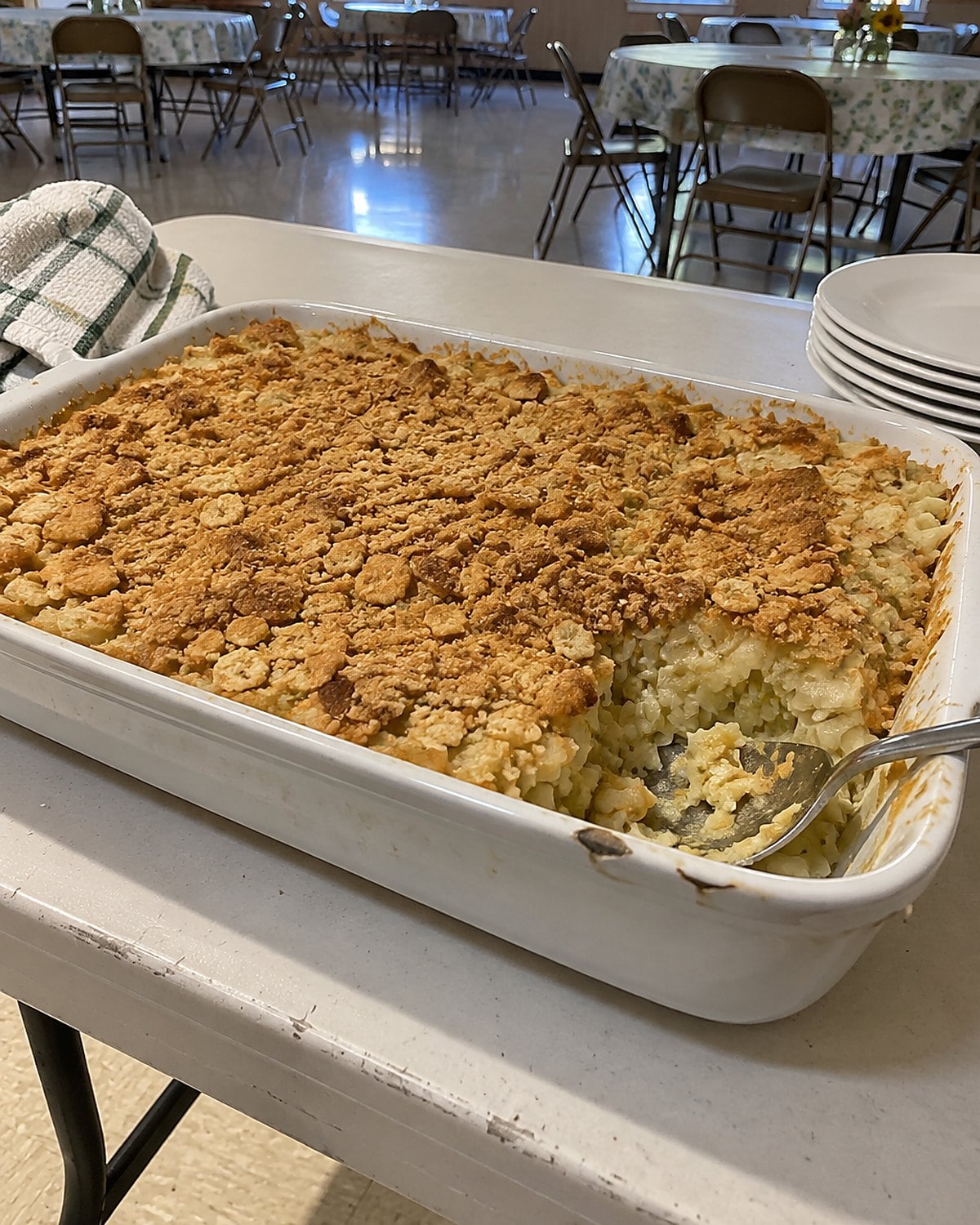 A cabbage casserole with a patchy cracker top sits uncovered on a church-hall folding table.