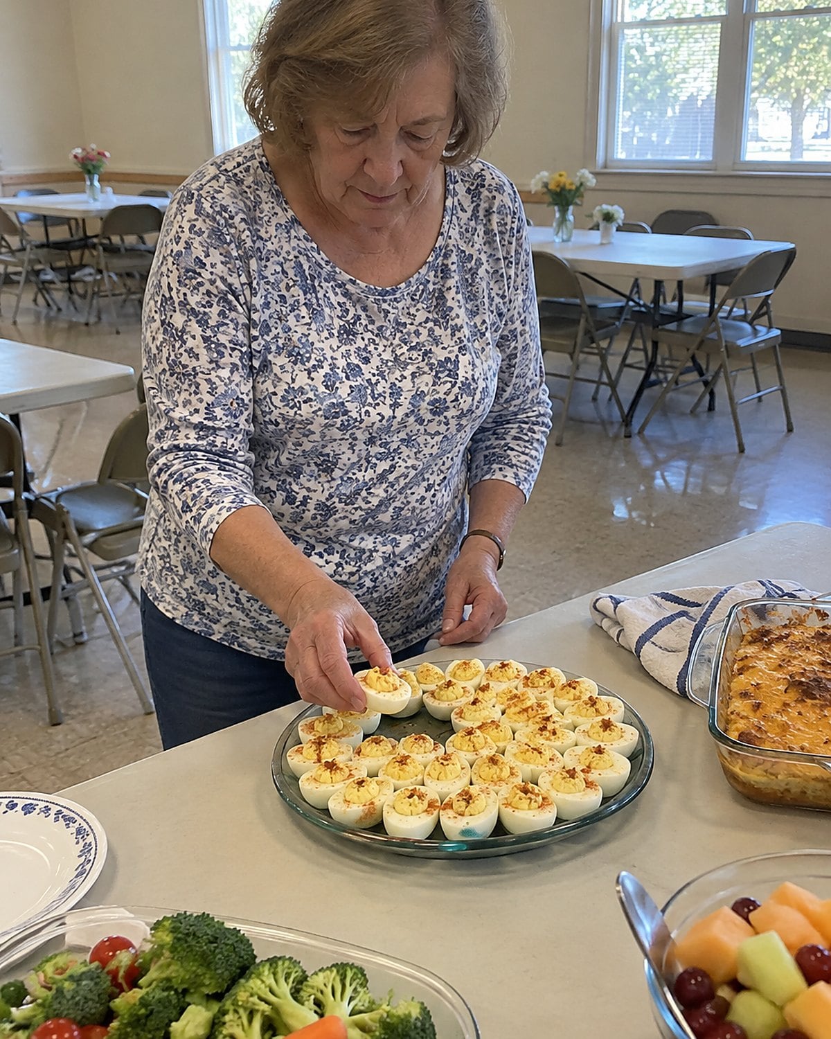 A hand lifts a deviled egg from a crowded tray on a church-hall folding table.