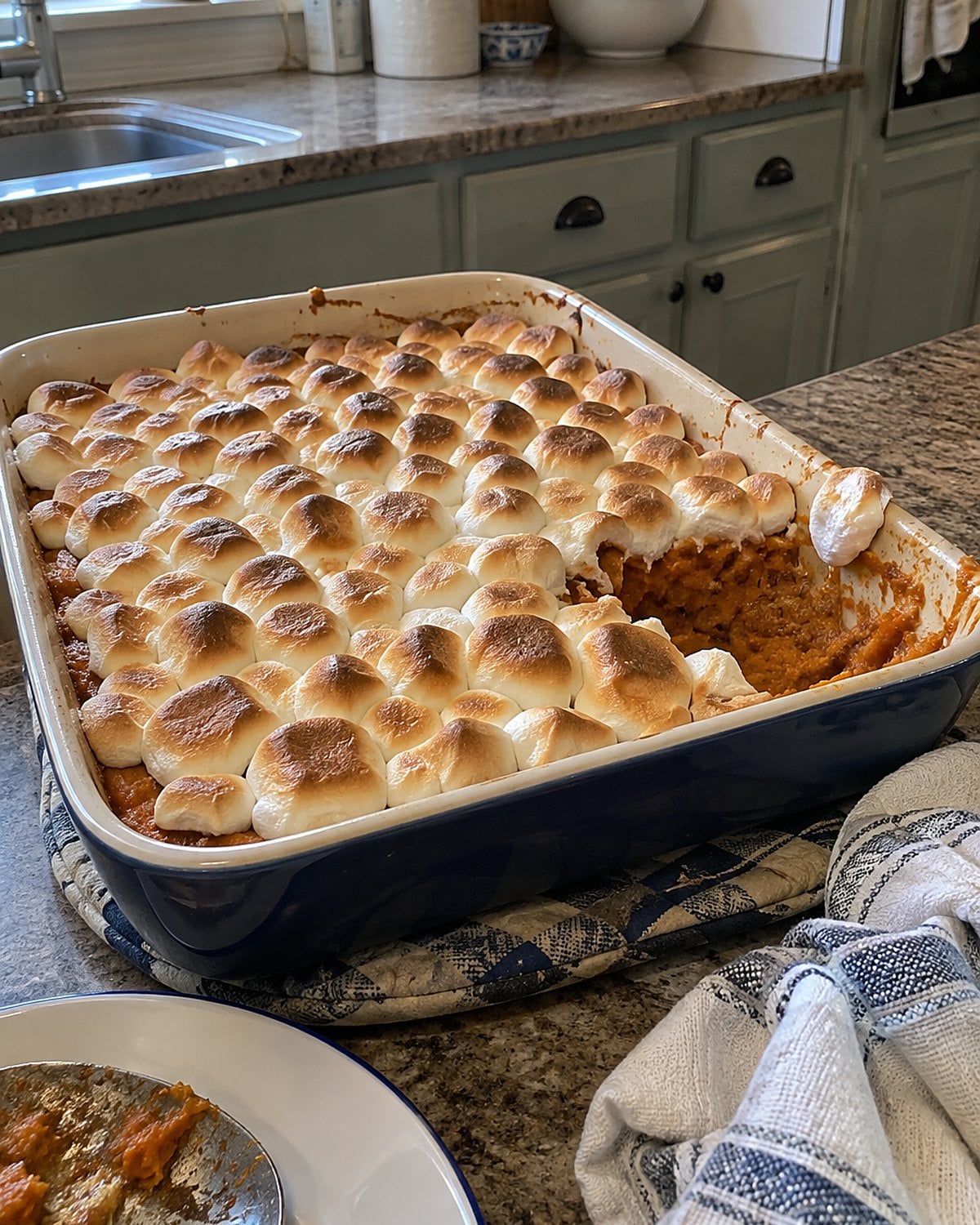 An unevenly toasted marshmallow topping covers a sweet potato casserole on a worn oven mitt.