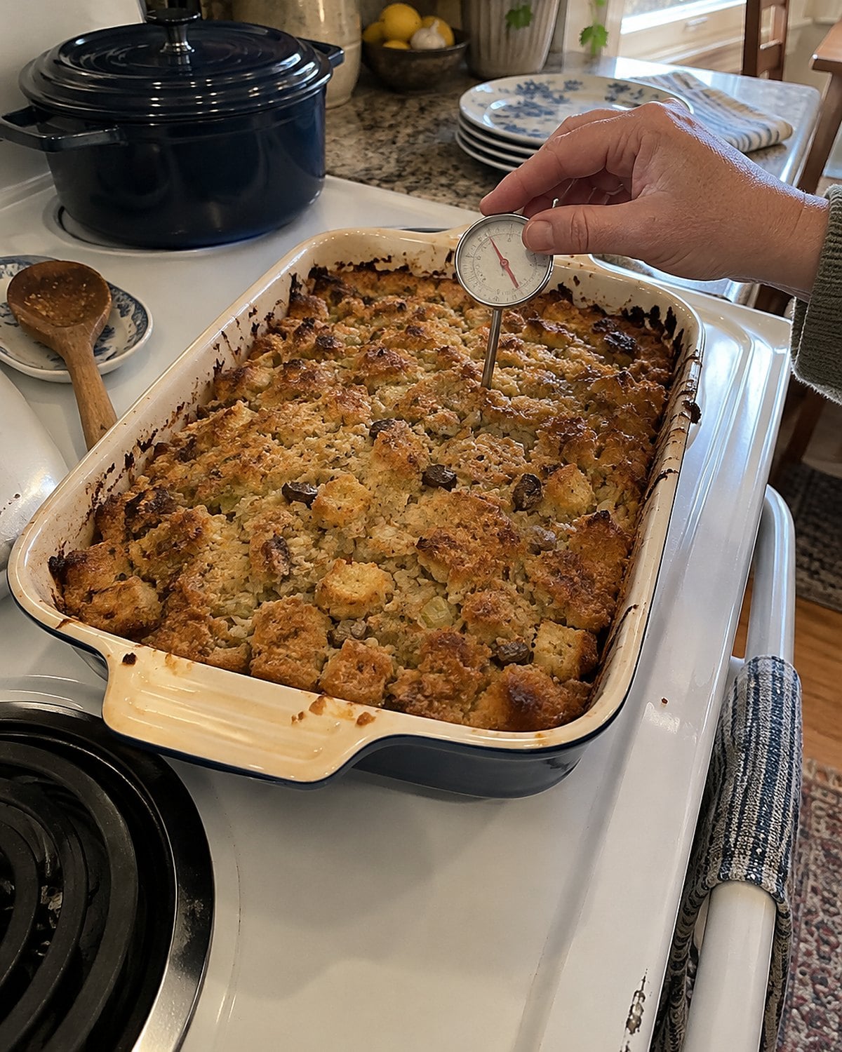 A browned oyster dressing in a baking dish sits on a stove with a thermometer inserted in its center.