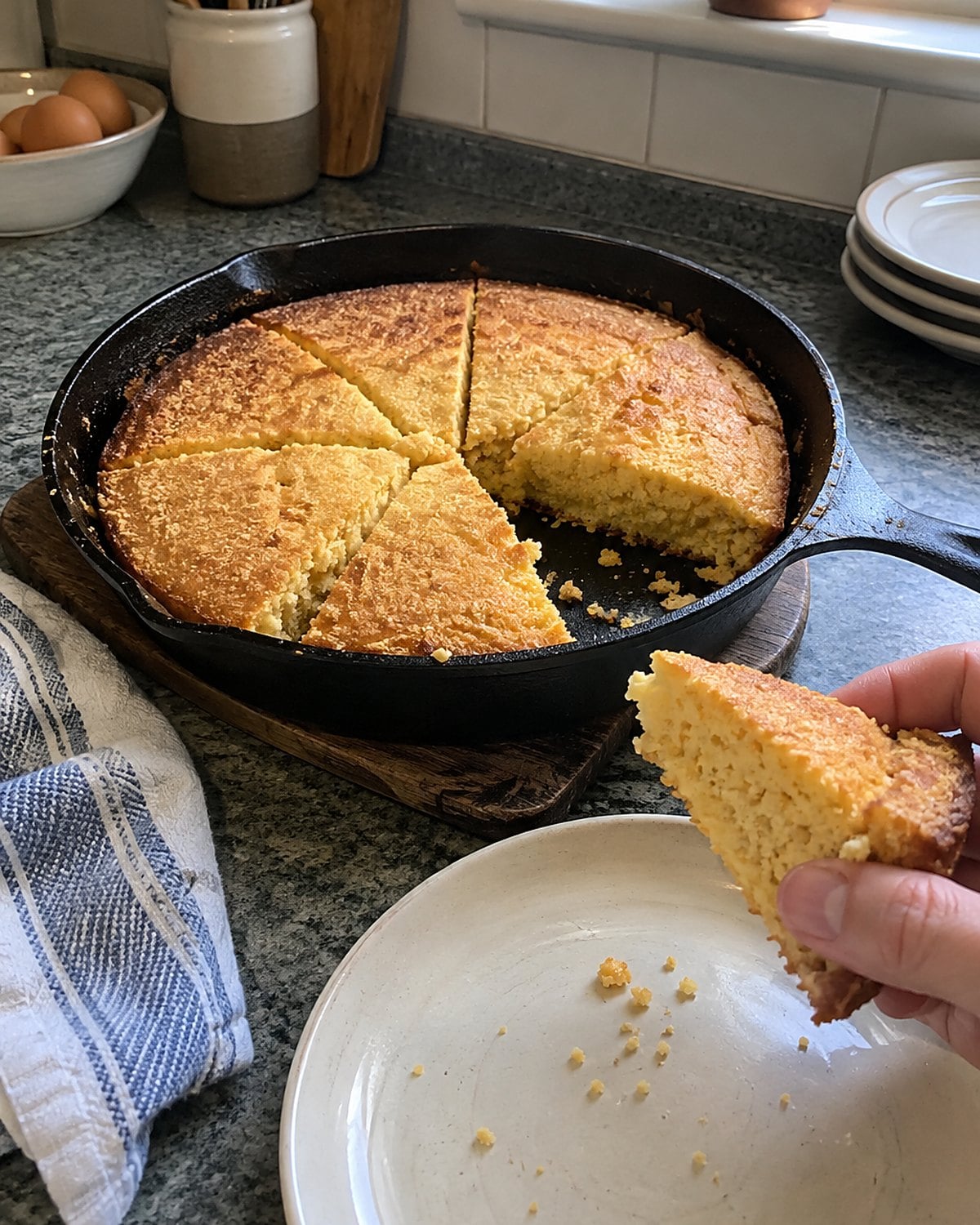 Uneven wedges of skillet cornbread sit in a cast-iron pan on a worn trivet.