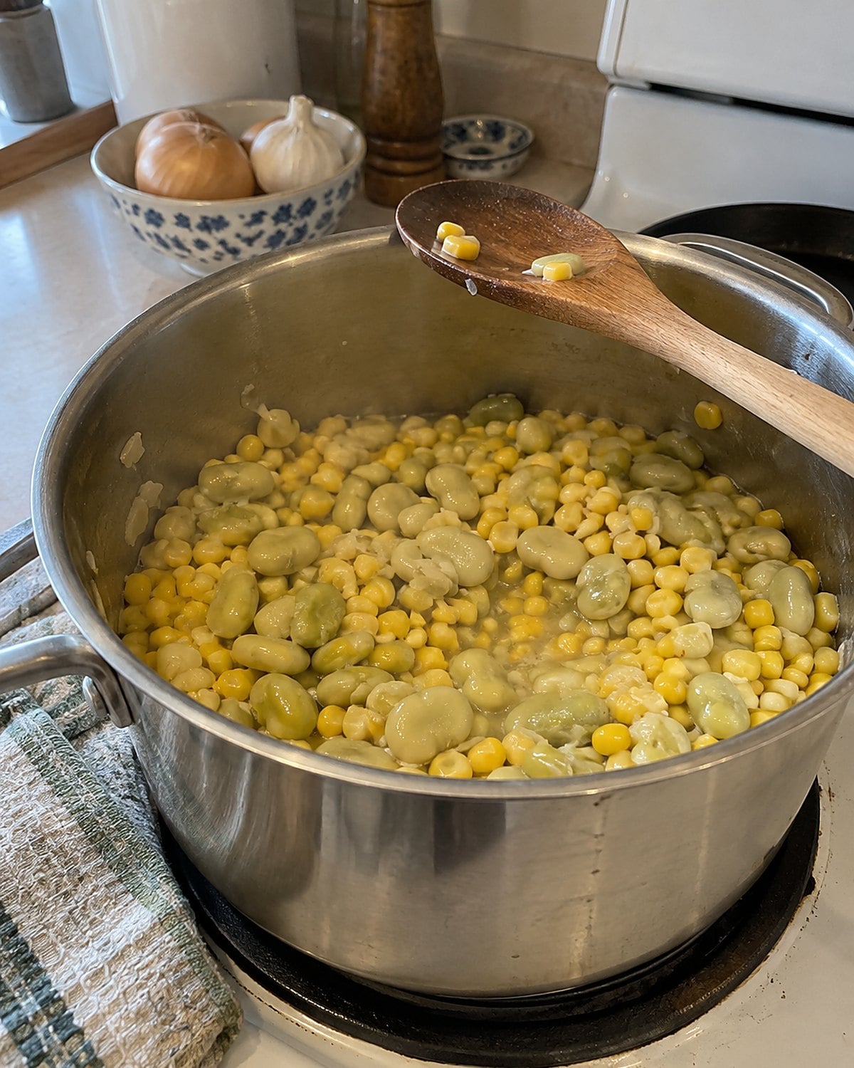 Lima beans and corn share a pot on the stove, with a wooden spoon resting across the rim.