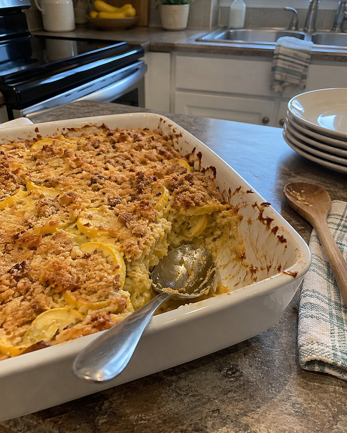 A spoon reaches the bottom of a squash casserole on the kitchen counter, with no liquid pooled in the gap.