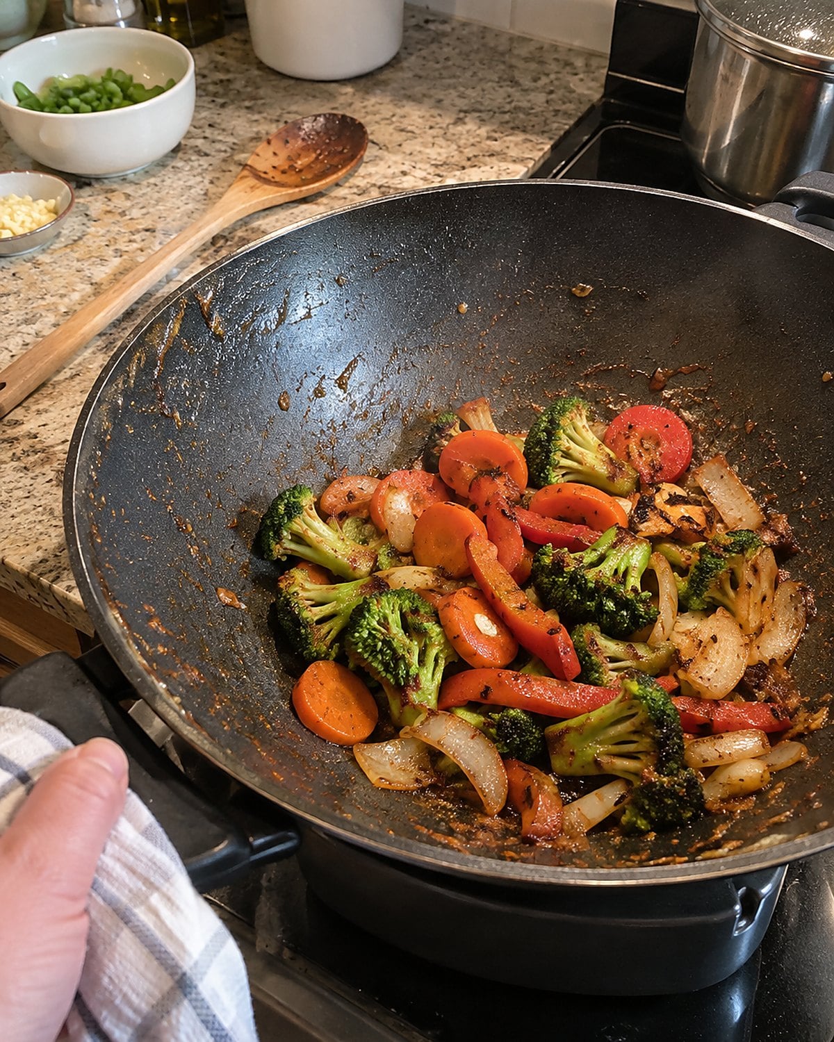 An electric wok with a small batch of vegetables browning beside a stove.