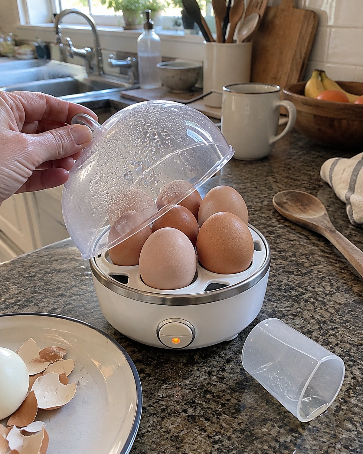 An electric egg cooker with its little cup beside it on a kitchen counter.