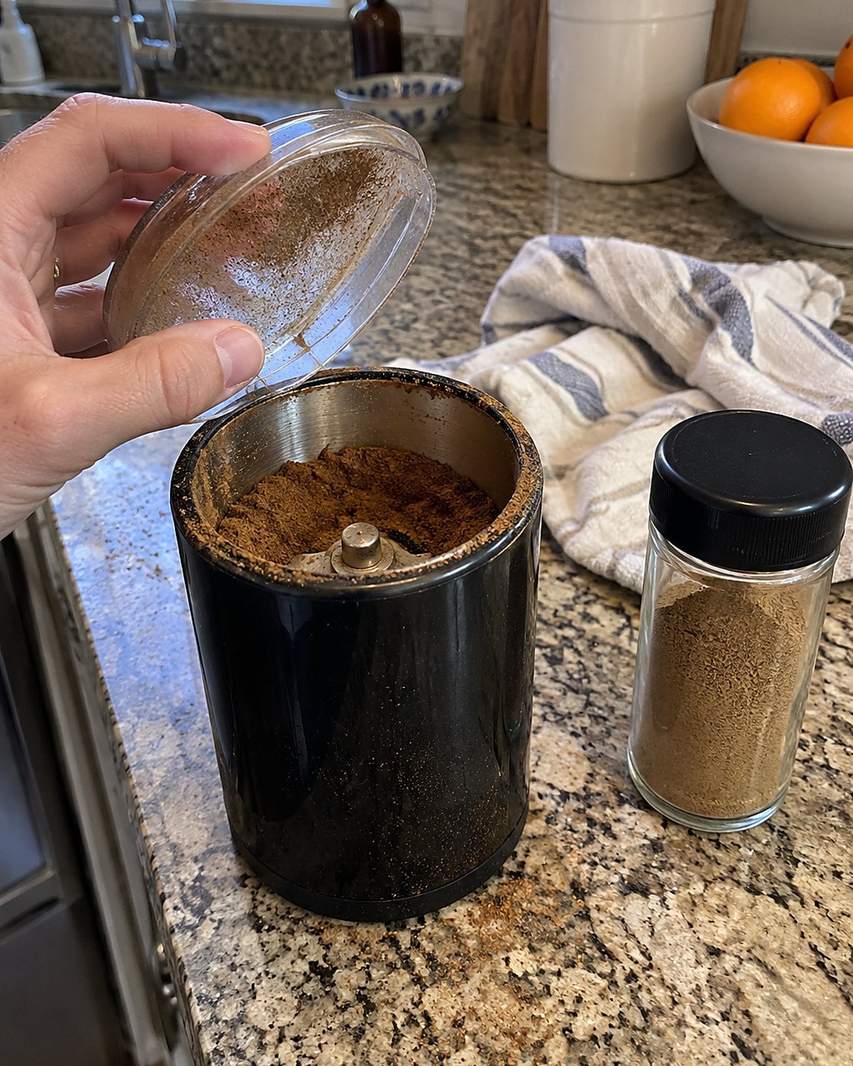 A small blade coffee grinder beside a spice jar on a flour-dusted kitchen counter.