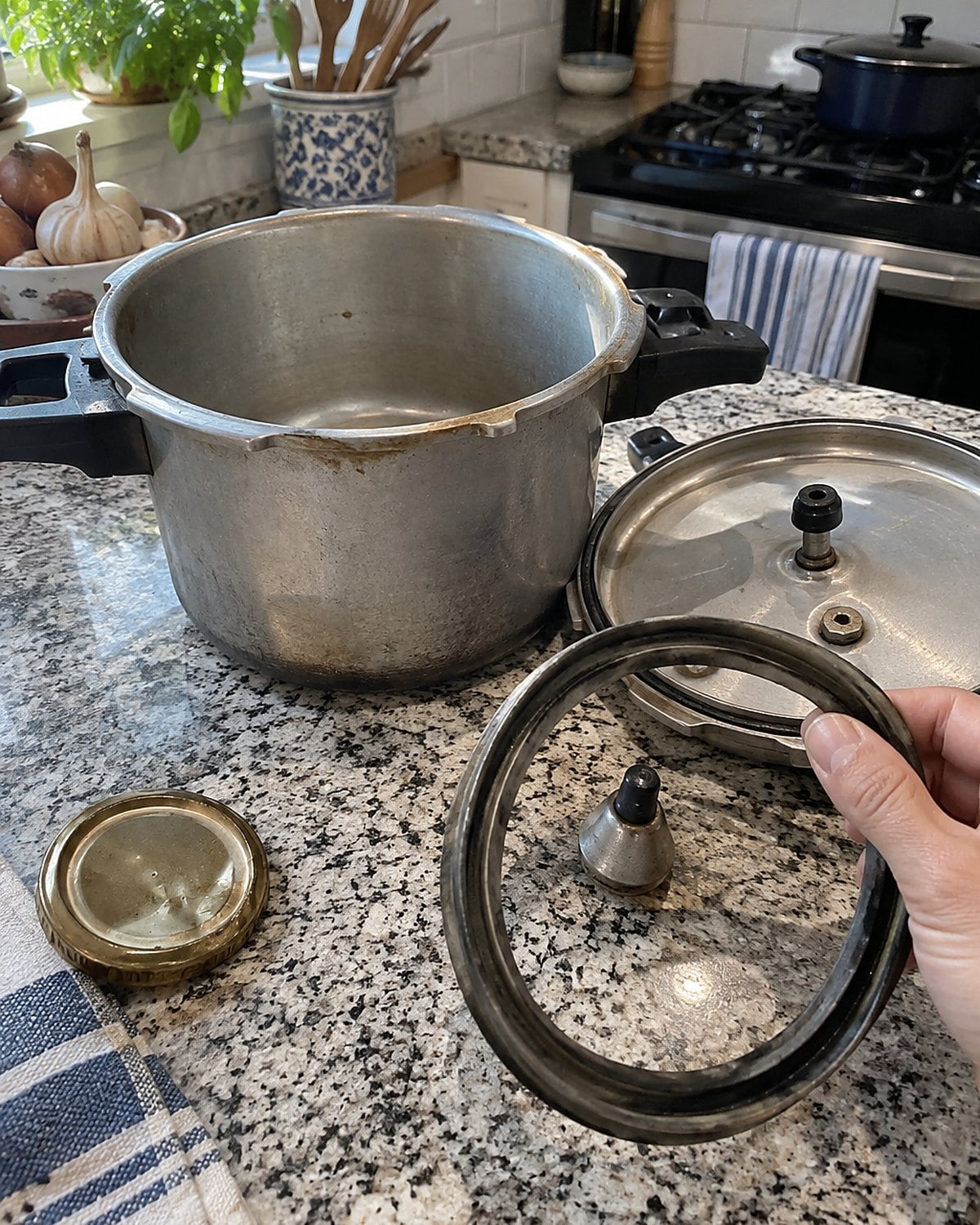 An old stovetop pressure cooker with its lid and gasket set apart on a counter.