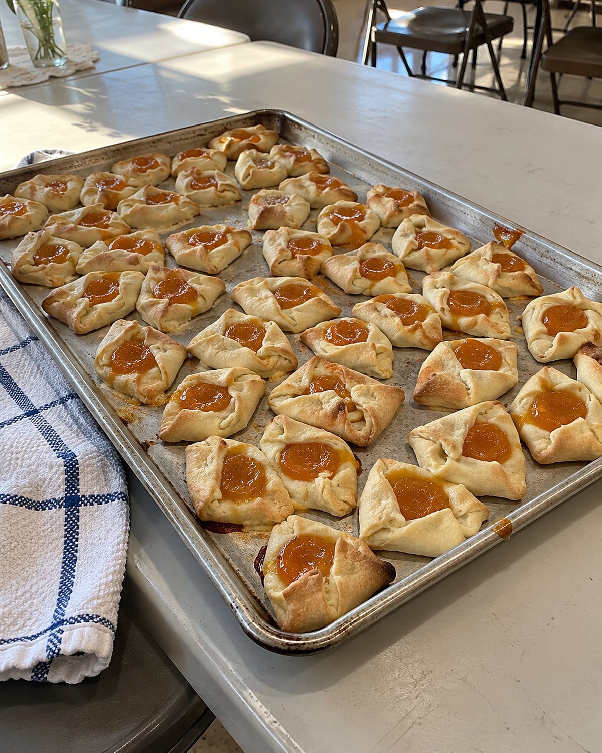 Apricot kolacky with uneven pinched corners fill a tray on a church hall table.