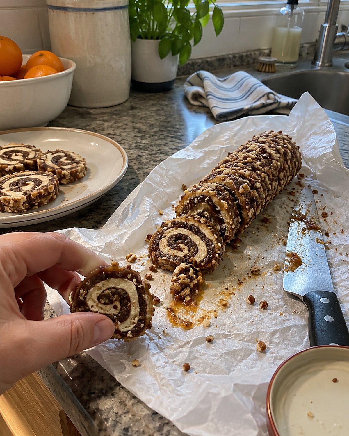 A sliced date pinwheel log sits on its wrapping paper beside a knife streaked with filling.