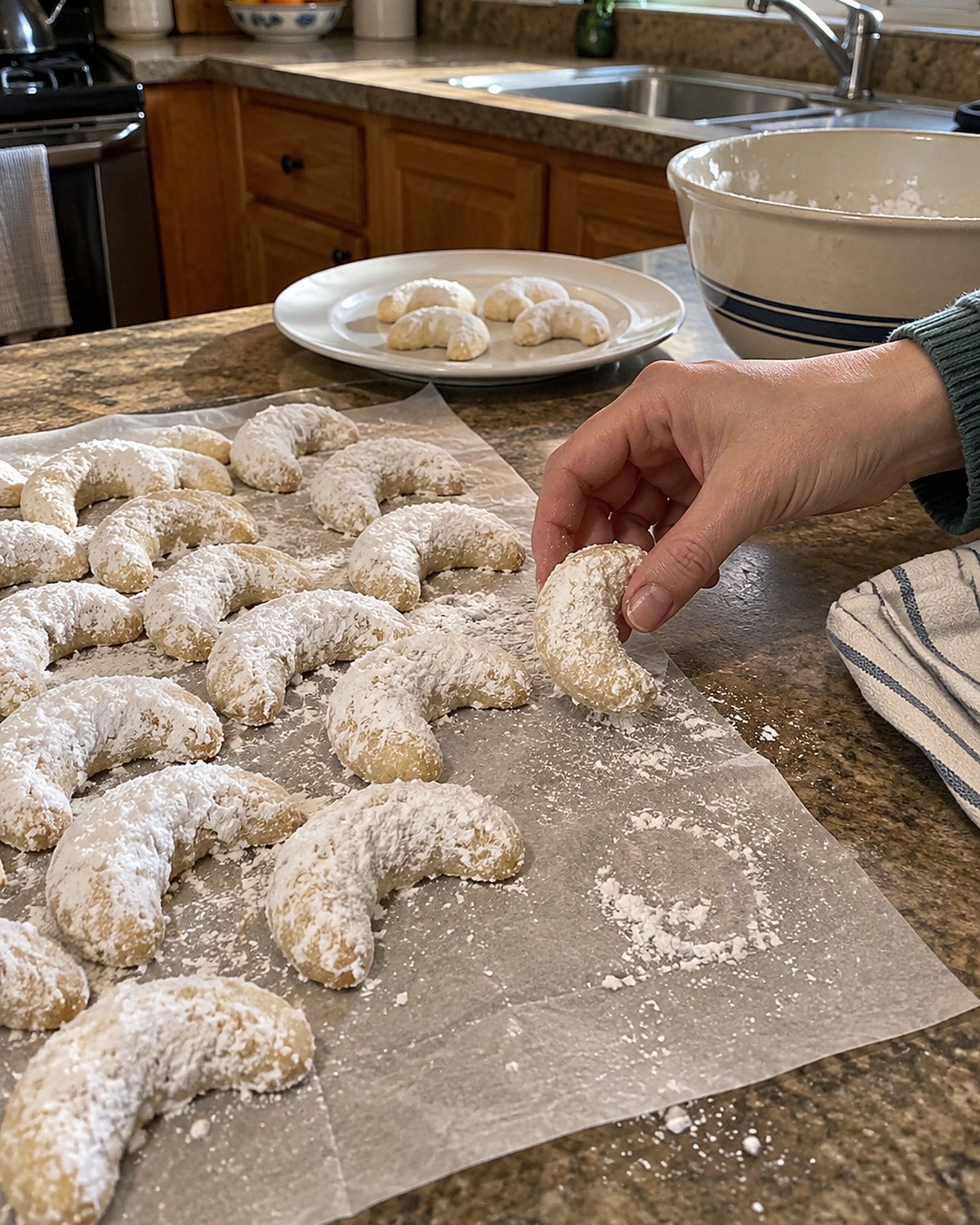 Powdered sugar crescents rest on wax paper with a white thumbprint on the edge of the sheet.
