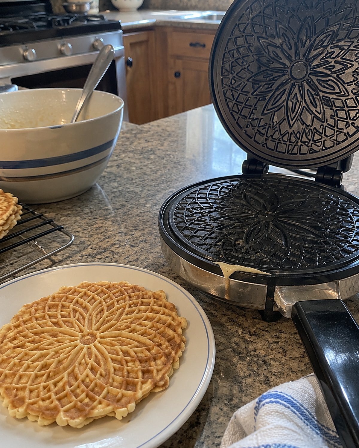 A patterned pizzelle cools beside an open iron with a little batter at its edge.