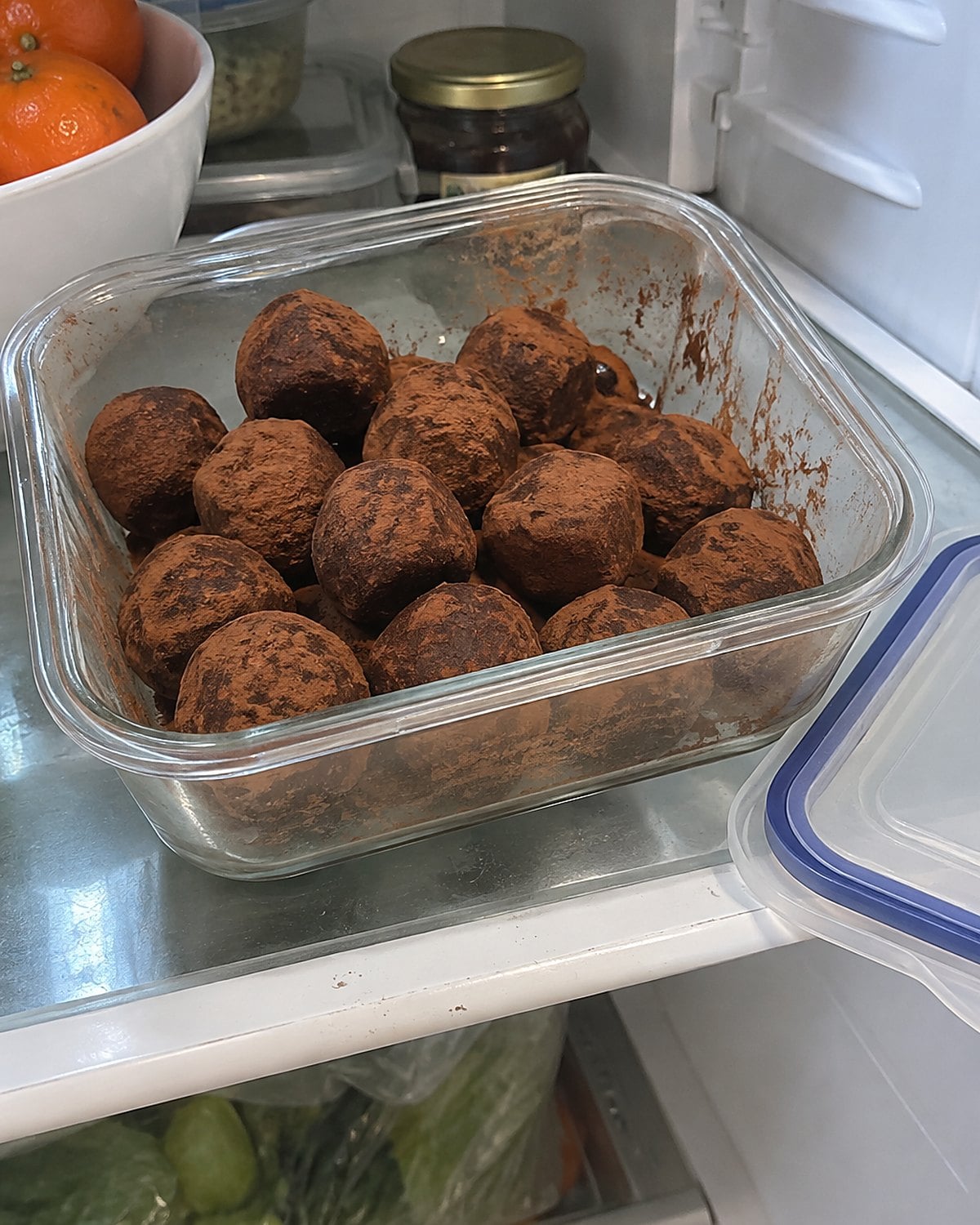A clearly labeled container of cocoa-dusted bourbon balls sits on a fridge shelf.