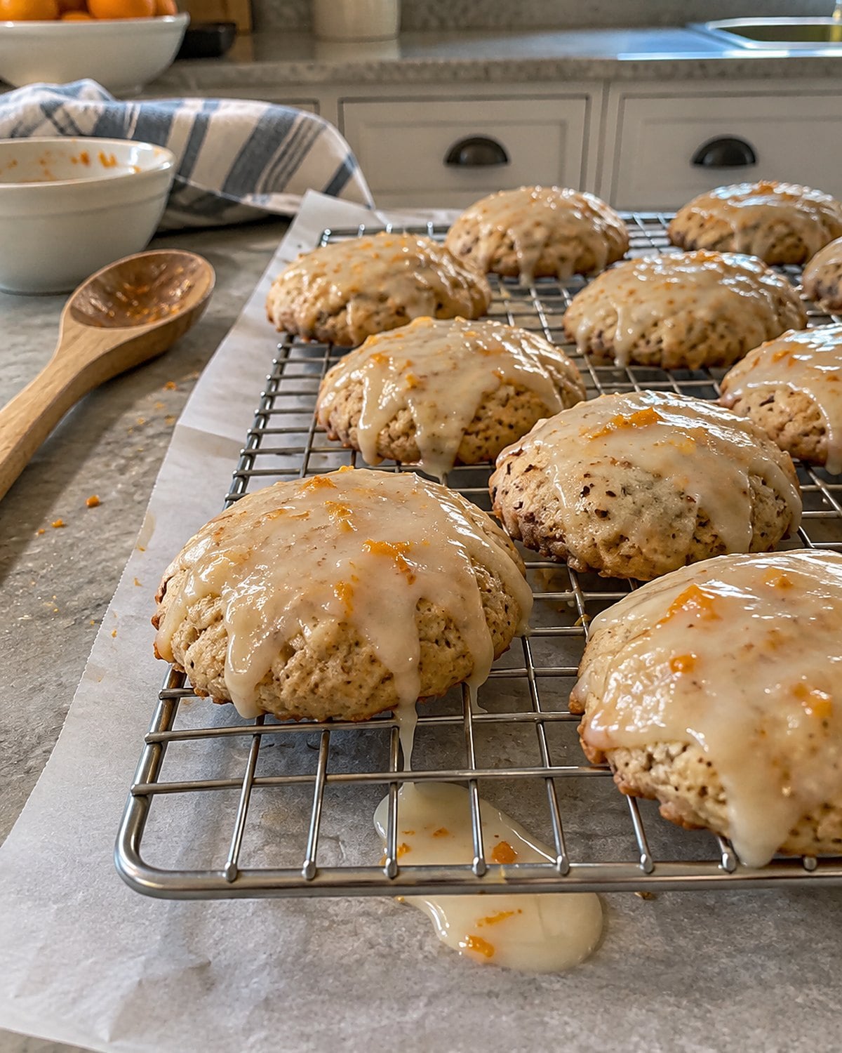 Orange glaze drips from anise cookies on a rack set over wax paper.