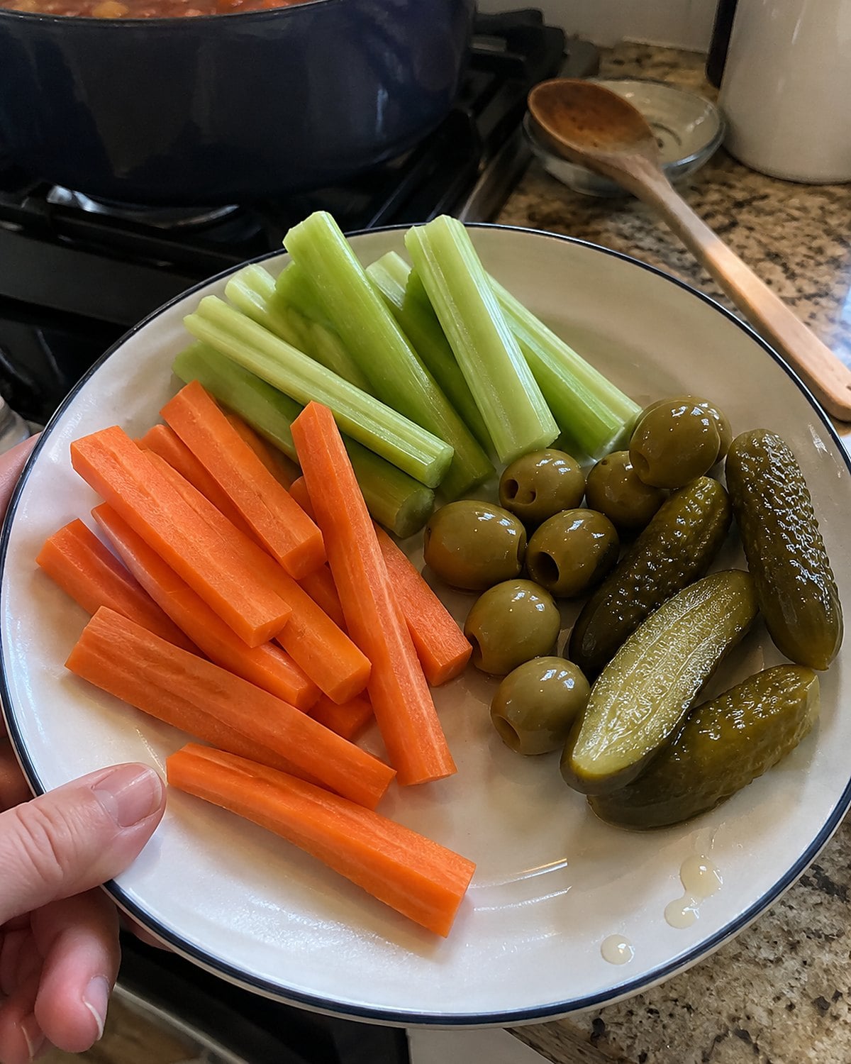 A small plate of carrot sticks, celery, olives, and pickles set near the stove while dinner cooks.