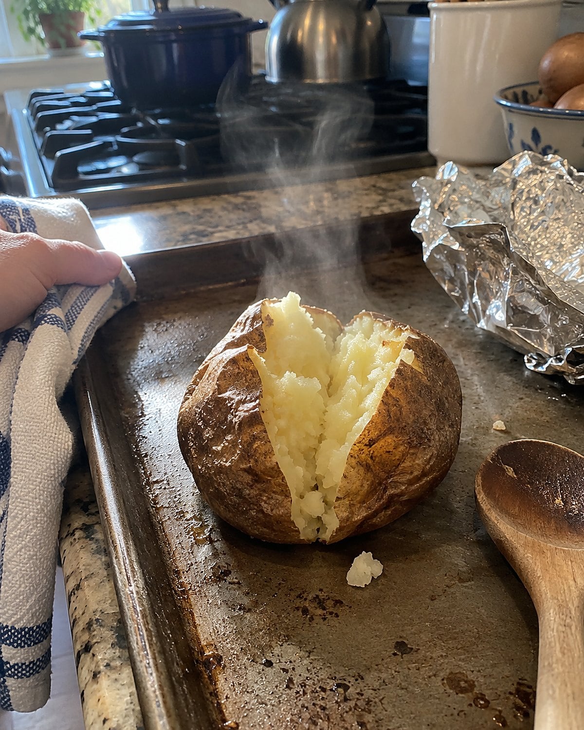 An unwrapped baked potato split open on a baking sheet beside discarded foil.