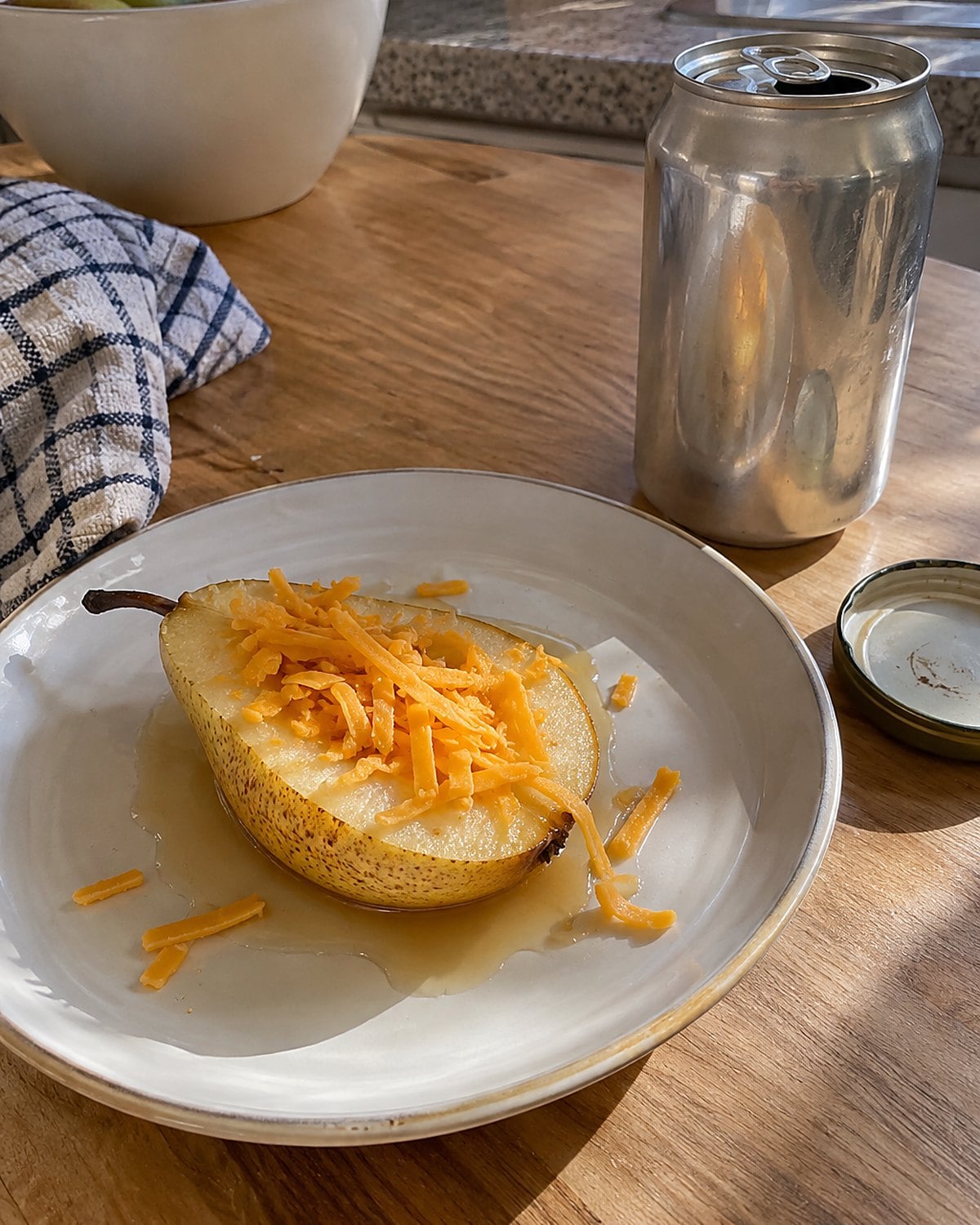A pear half with grated cheddar on a small lunch plate beside an opened can.
