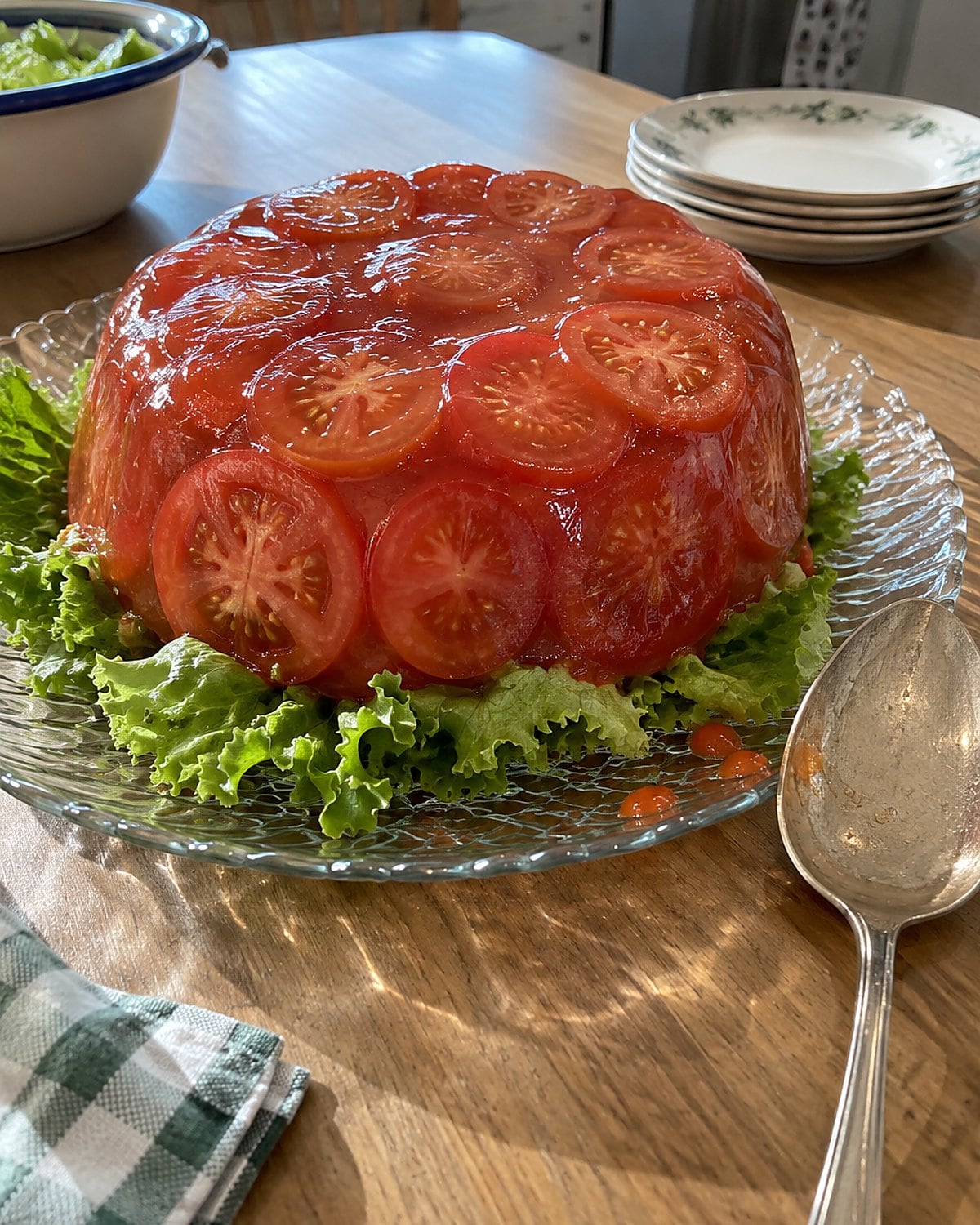 Tomato aspic on lettuce, slightly off-center on a glass plate at a dining table.