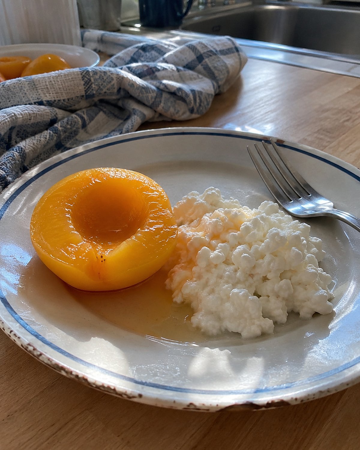 A drained peach half beside a scoop of cottage cheese on a chipped lunch plate.