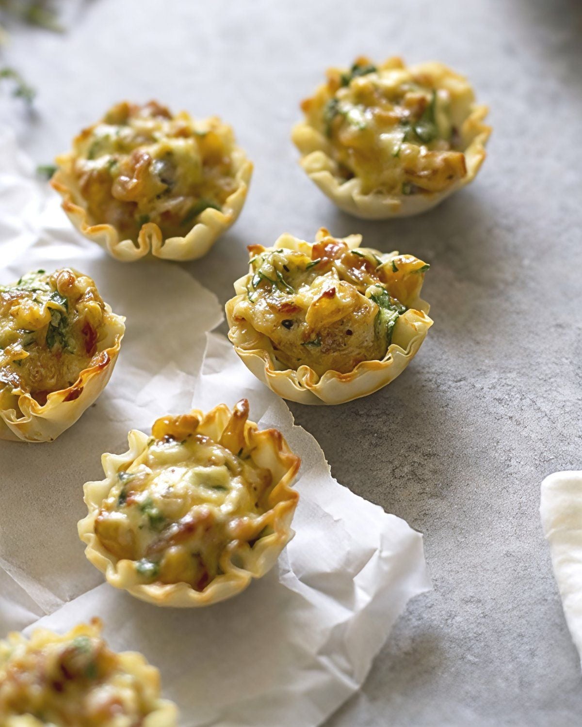 Crispy, mini phyllo pastry cups filled with savory, melted cheese and caramelized French onion mixture are arranged on parchment paper.