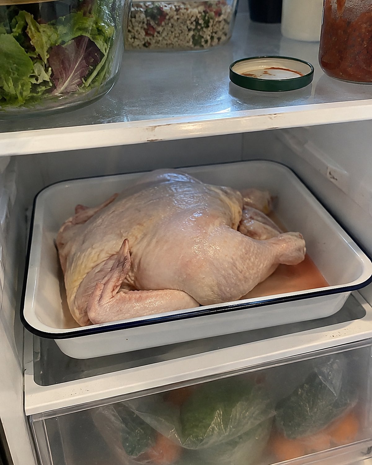 A package of raw chicken sits in a rimmed tray on the bottom refrigerator shelf.