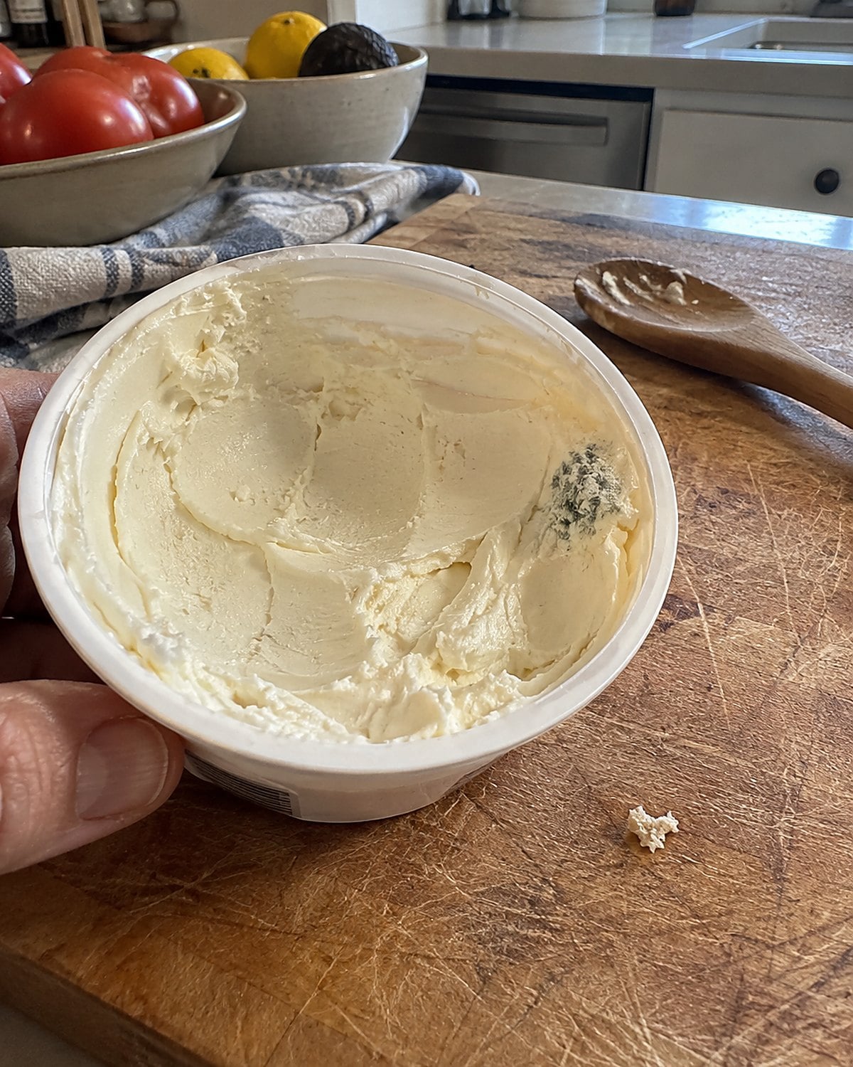 An opened tub of soft cheese with a fuzzy edge rests on a cutting board.
