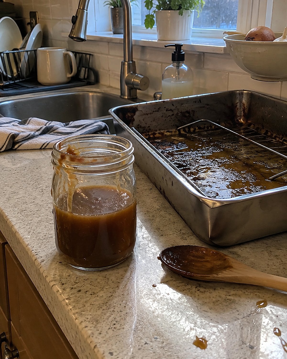 A small jar of gravy stands beside a roasting pan waiting to be washed at the sink.