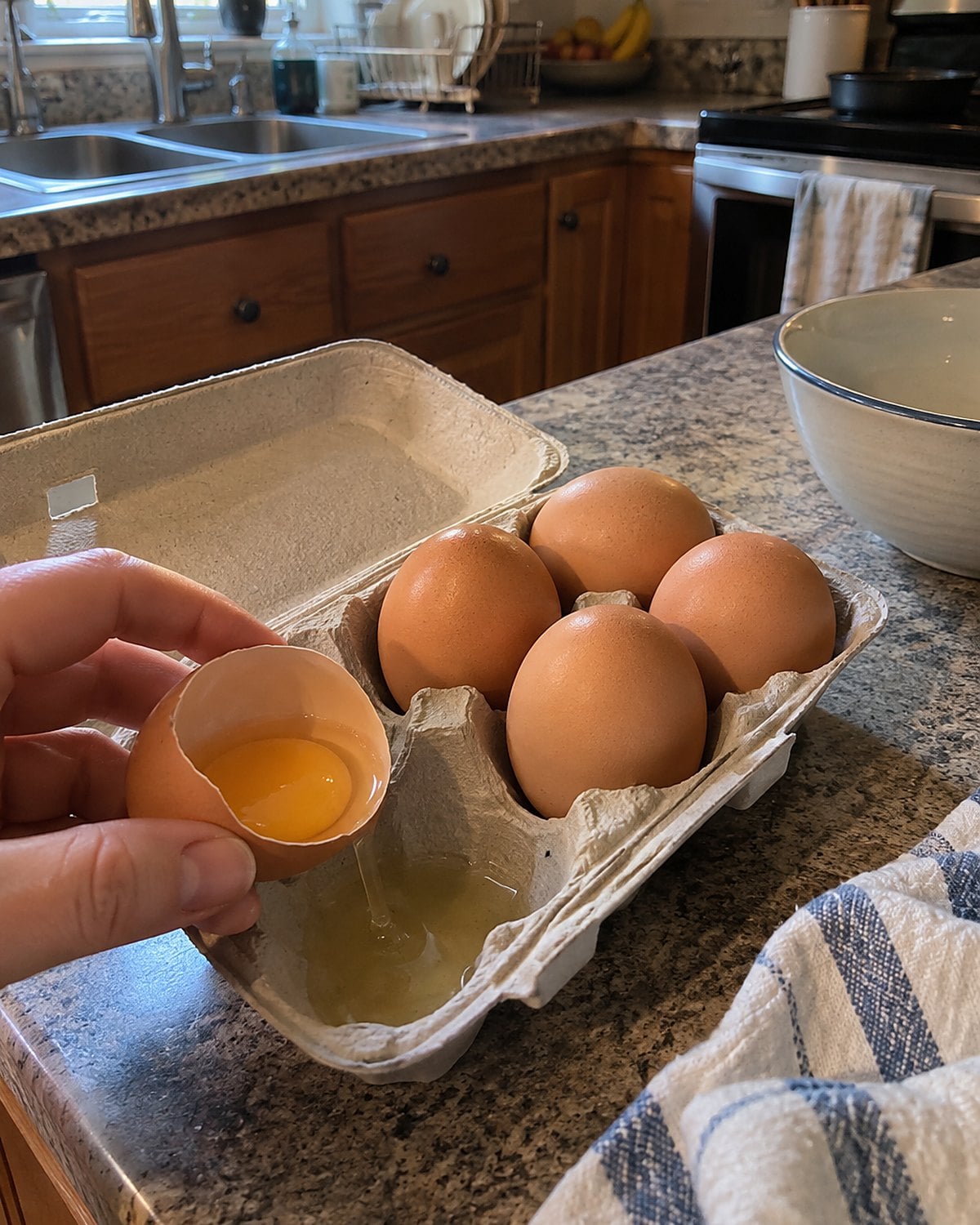A cracked egg sits in an open carton on the kitchen counter.
