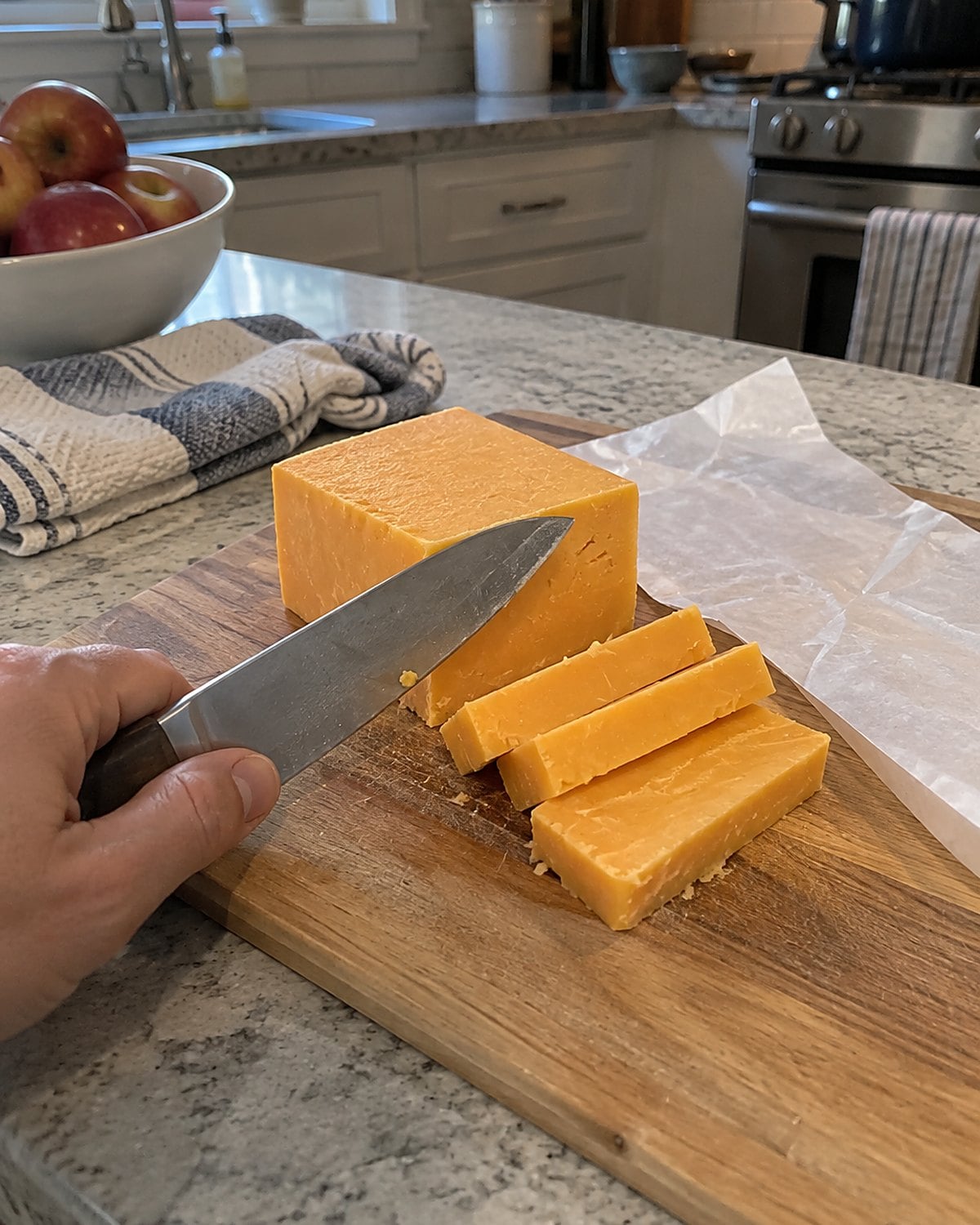 A clean, dry knife and a partly cut cheddar block sit beside fresh wrapping on a wooden board.