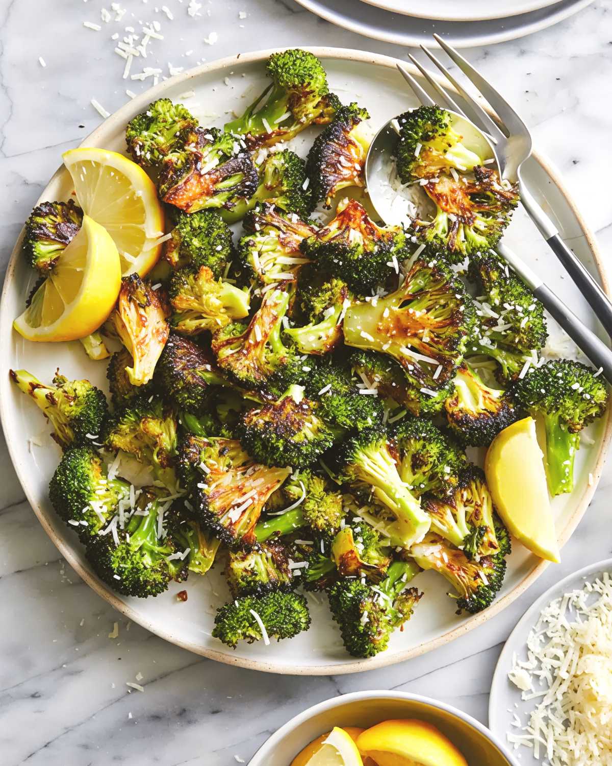 Crisp garlic parmesan roasted broccoli florets sprinkled with shredded Parmesan cheese and served with fresh lemon wedges on a platter, ideal for easy last minute potluck ideas.