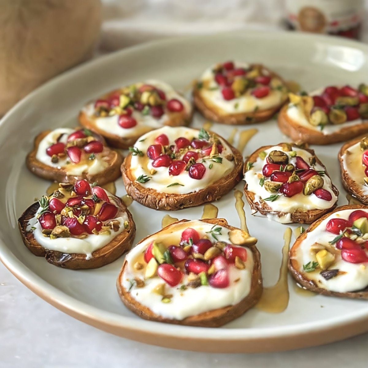 Roasted sweet potato rounds topped with creamy ricotta, pomegranate seeds, chopped pistachios, and honey drizzle on a white plate, perfect for festive gluten free thanksgiving appetizers.