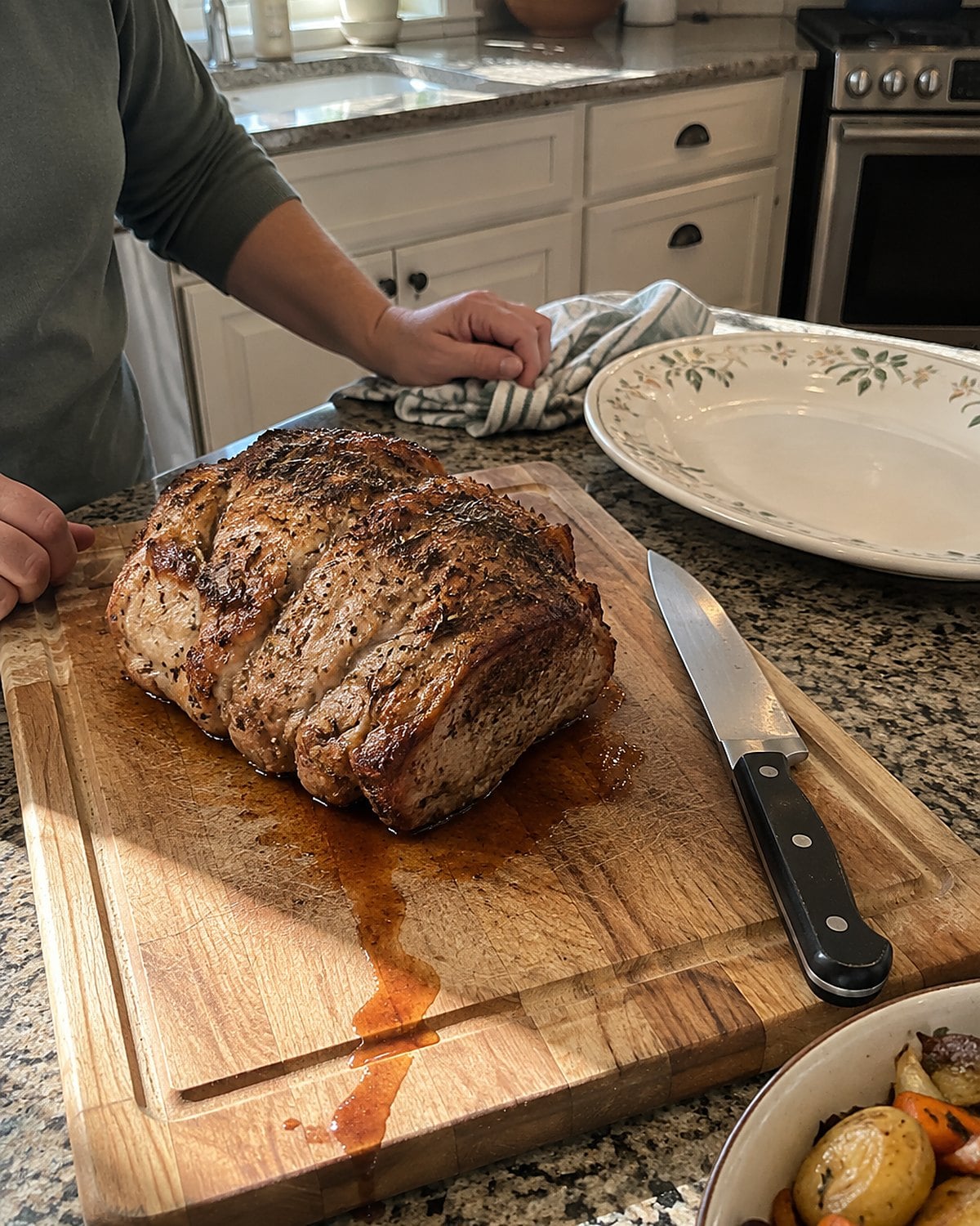 A pork roast on a cutting board beside an unused carving knife and a serving platter.