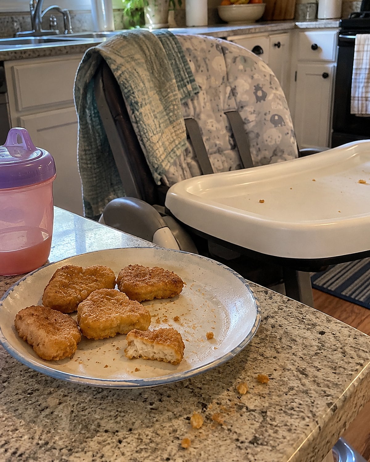 Chicken nuggets cooling on a small plate beside a grandchild's high chair.