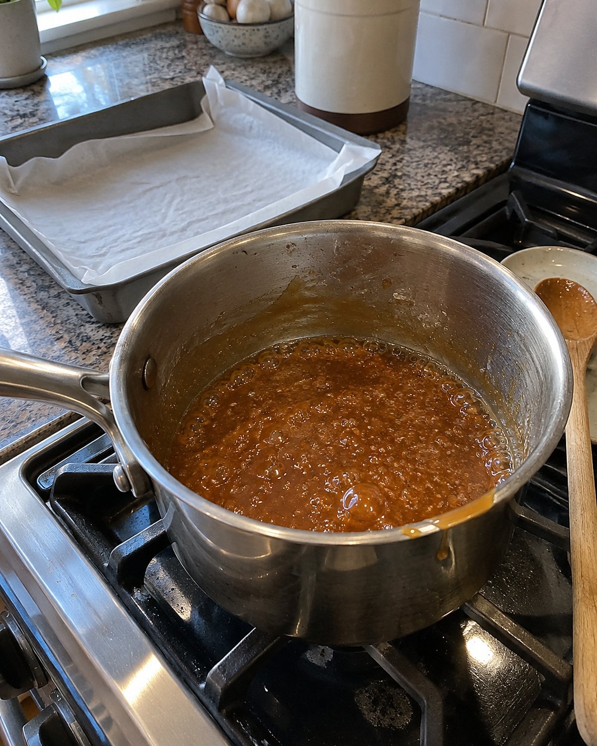 Amber caramel in a heavy saucepan beside a waiting lined pan on a home stove.