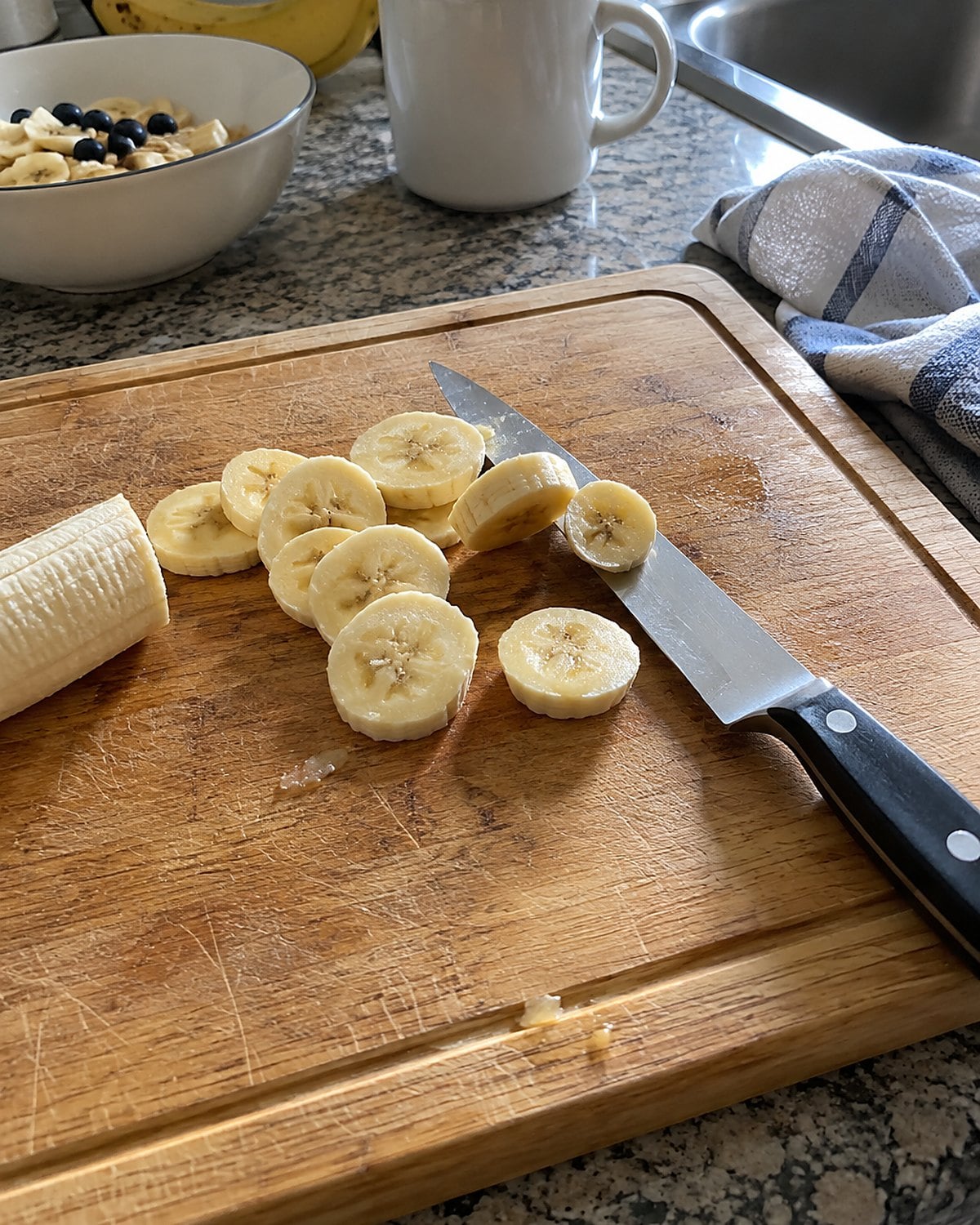 A table knife lying flat on a cutting board beside uneven banana slices.