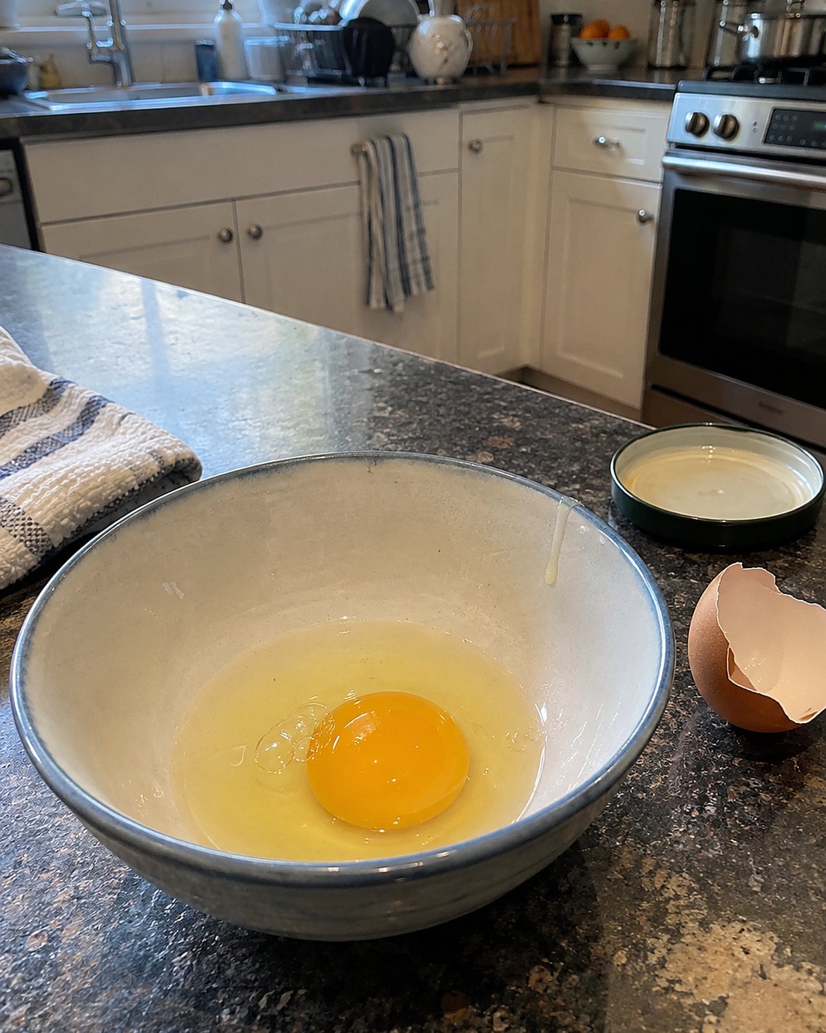 A cracked egg in a small bowl on the counter, with a bit of shell beside it.