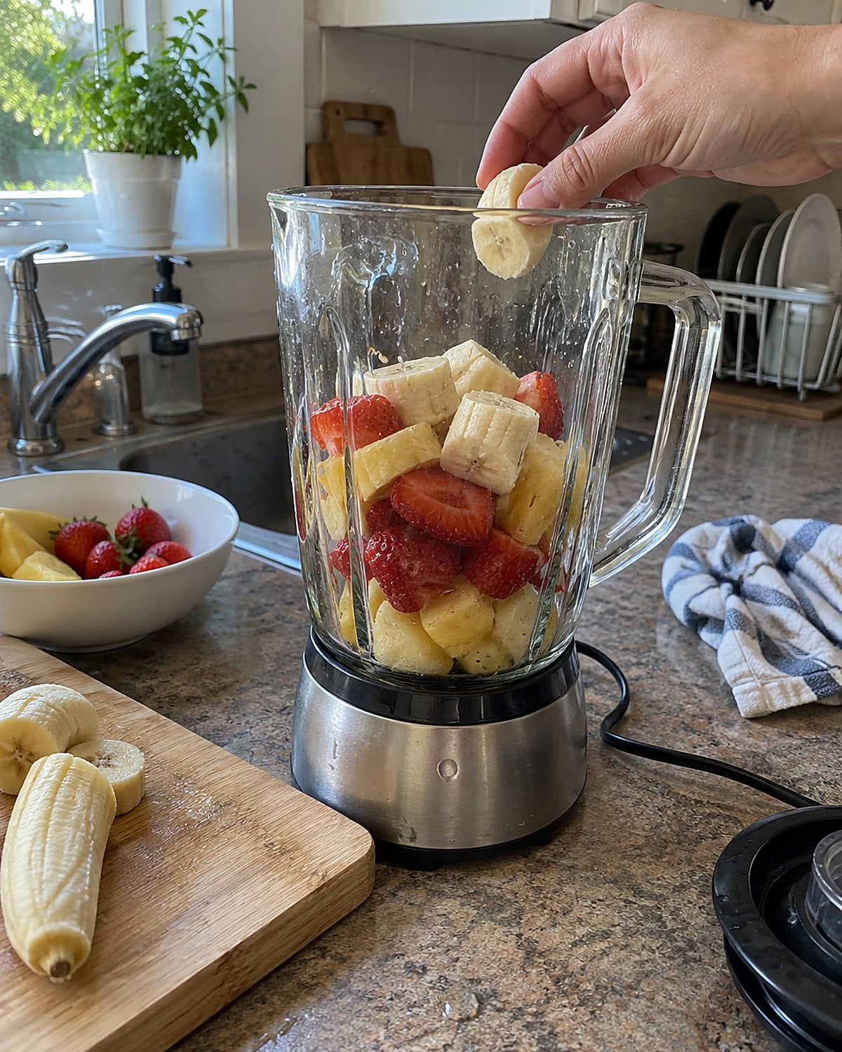 An unplugged blender jar with fruit inside, sitting beside its cord on the counter.