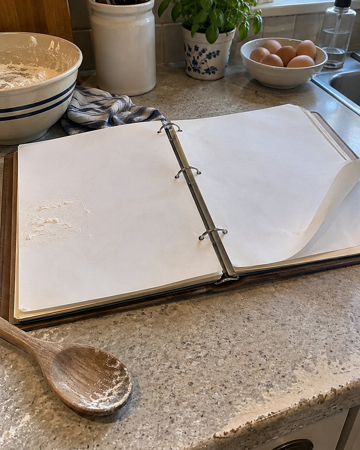 A worn church cookbook lies open on a counter, with flour on the page and a loose corner curling up.