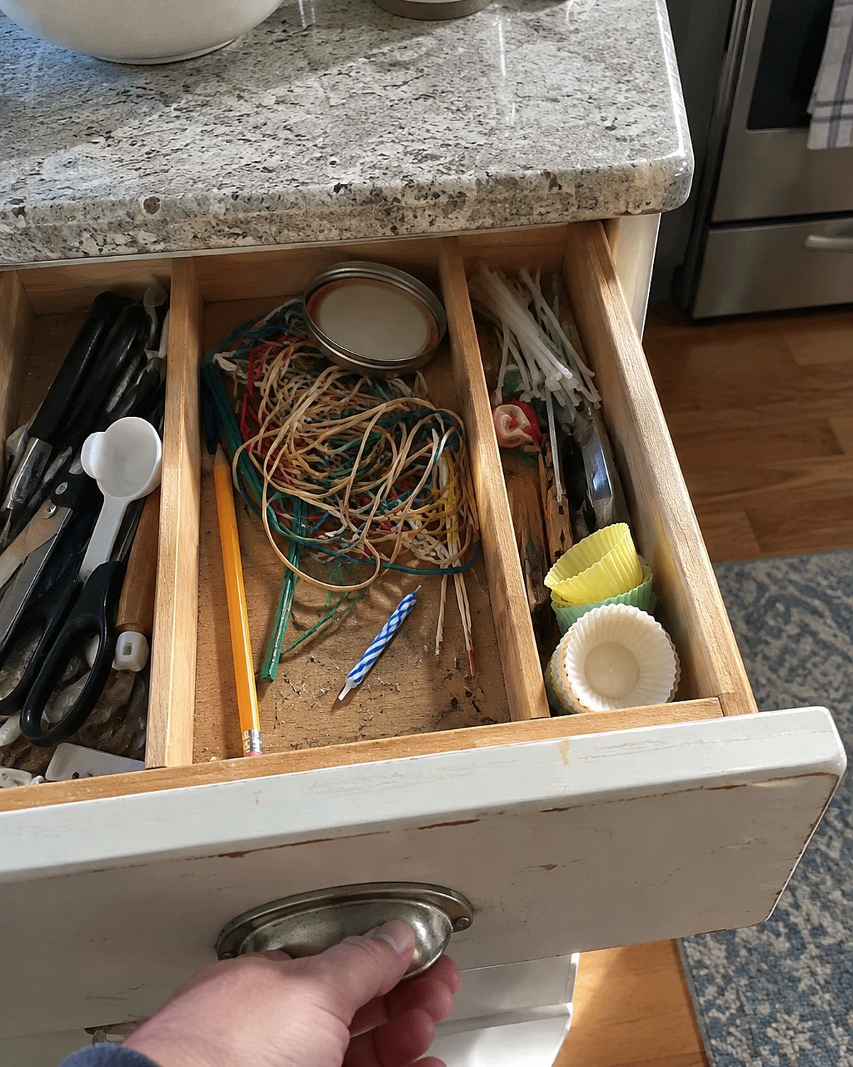 An open kitchen drawer holds twist ties, rubber bands, a pencil, and a loose birthday candle.