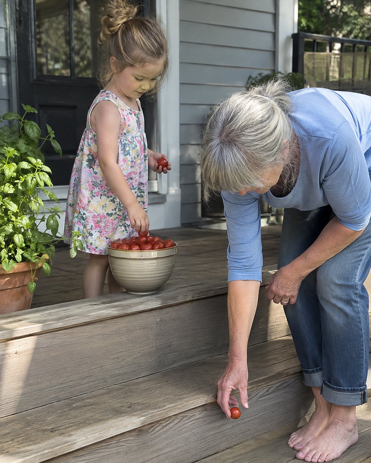 A bowl of cherry tomatoes sits on a porch step, with a grandchildโs hand adding another tomato.