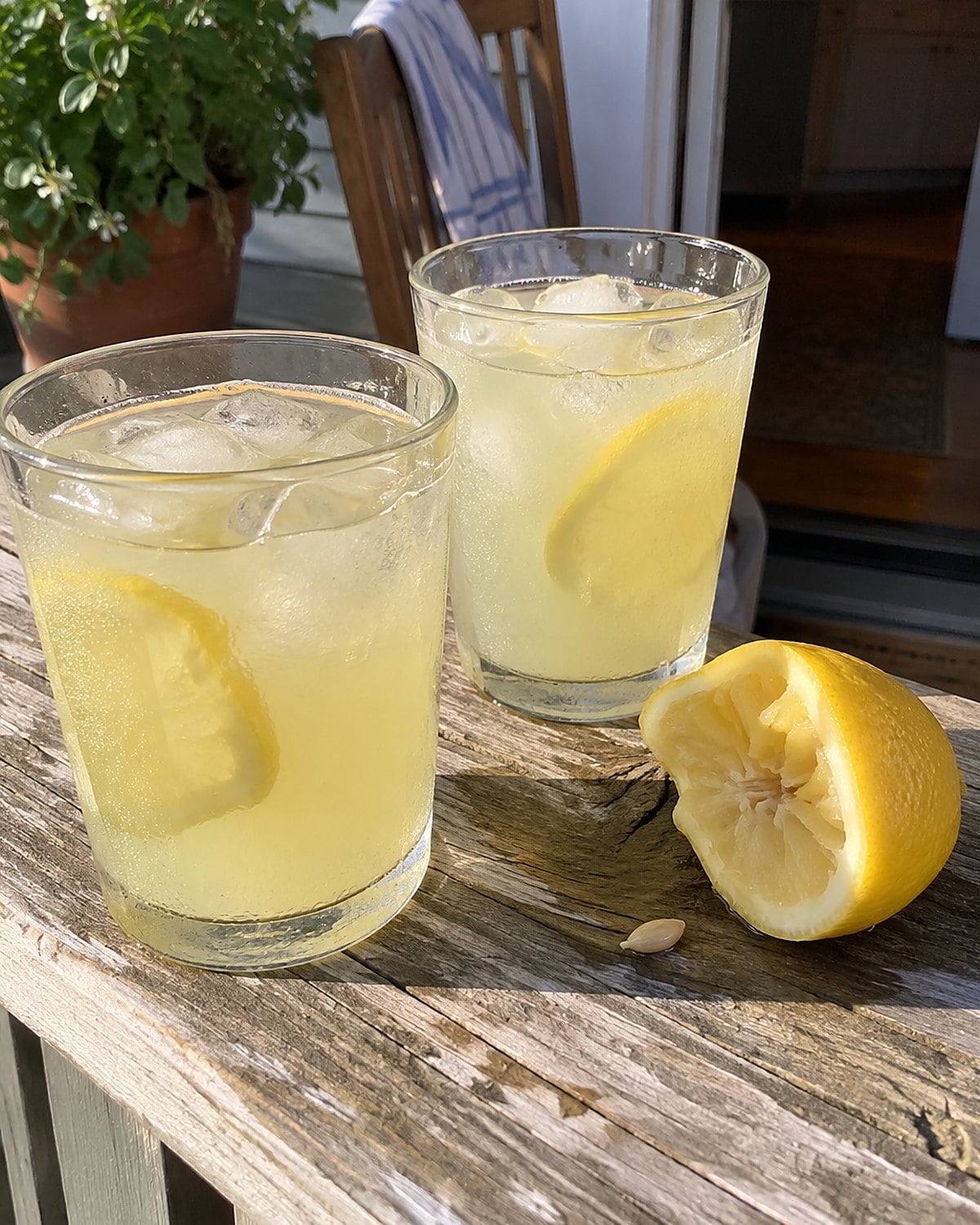 Two sweating glasses of lemonade on a porch rail beside a squeezed lemon.