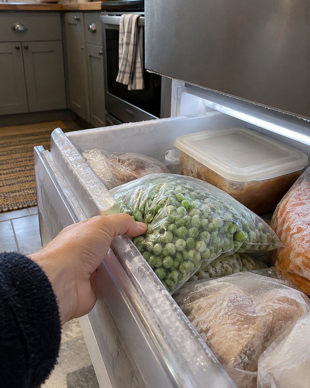 An open freezer drawer with a labeled supper container tucked behind a bag of peas.