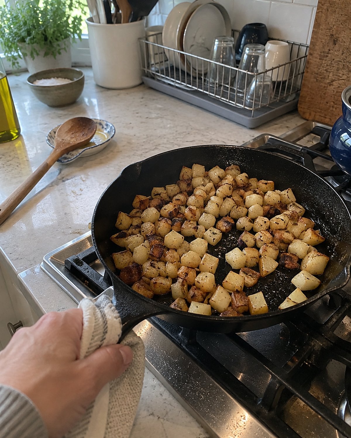 Cubed potatoes browning in a worn cast-iron pan on a home stove.