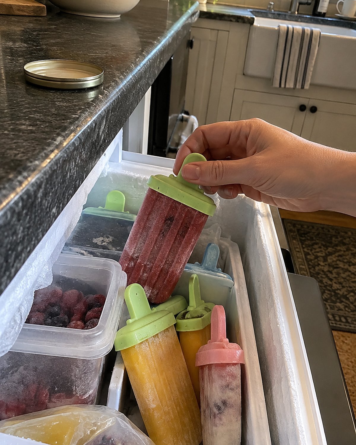 A freezer drawer pulled open to show homemade ice pops in mismatched molds.