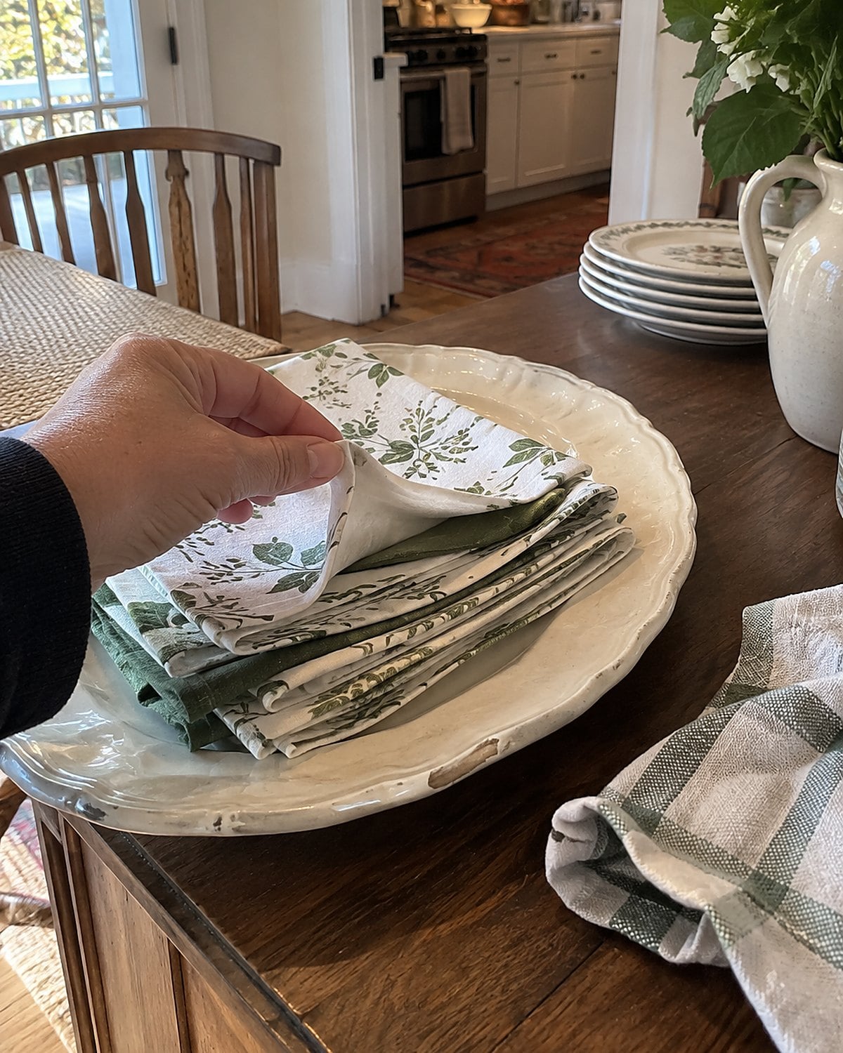 A chipped serving platter holds a stack of folded napkins on a sideboard.