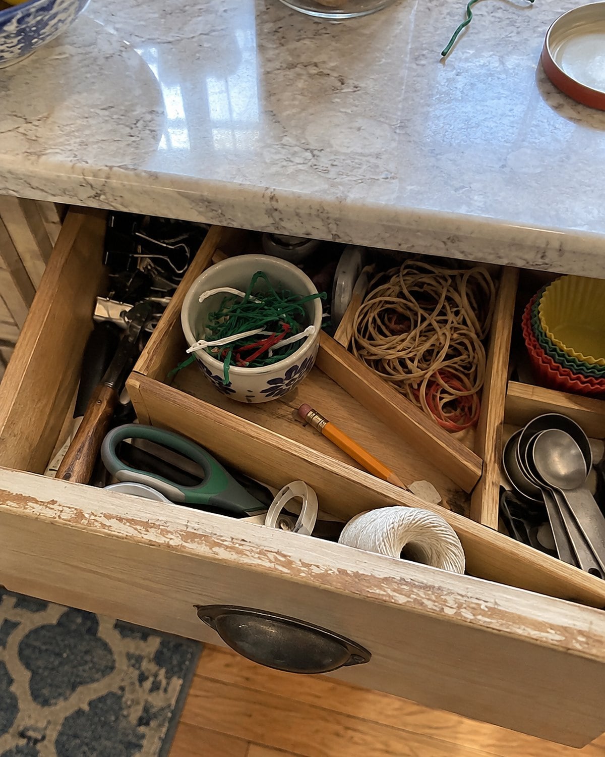 An open kitchen drawer holds twist ties in a small cup beside a rubber band and pencil stub.
