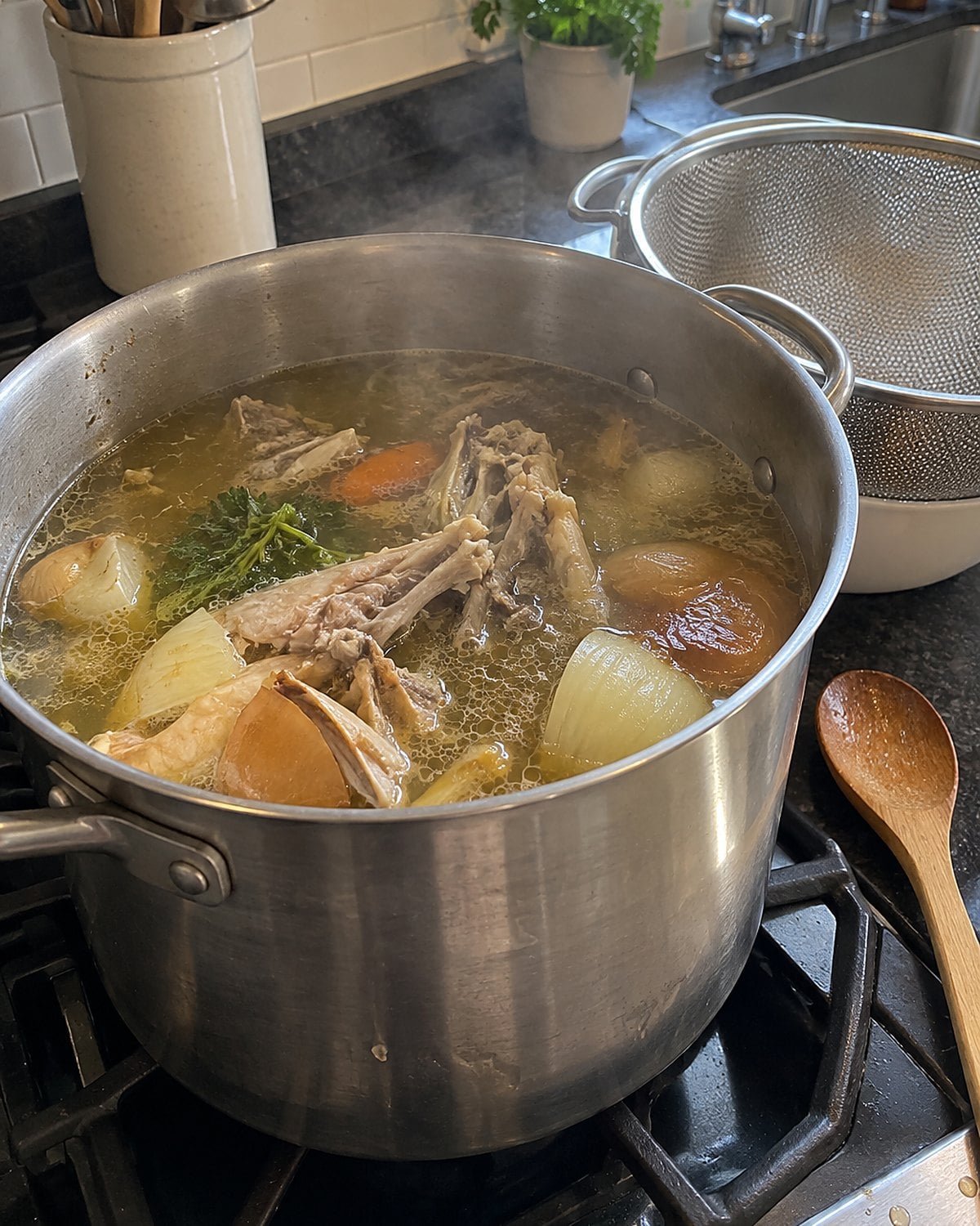 A stockpot holding chicken bones and onion ends sits beside a strainer on the stove.