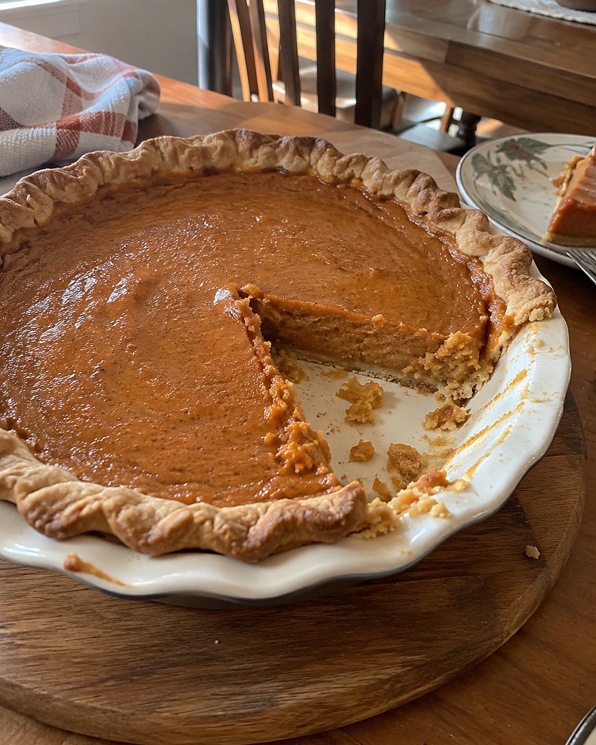 A sweet potato pie with one uneven slice missing on a Thanksgiving serving board.