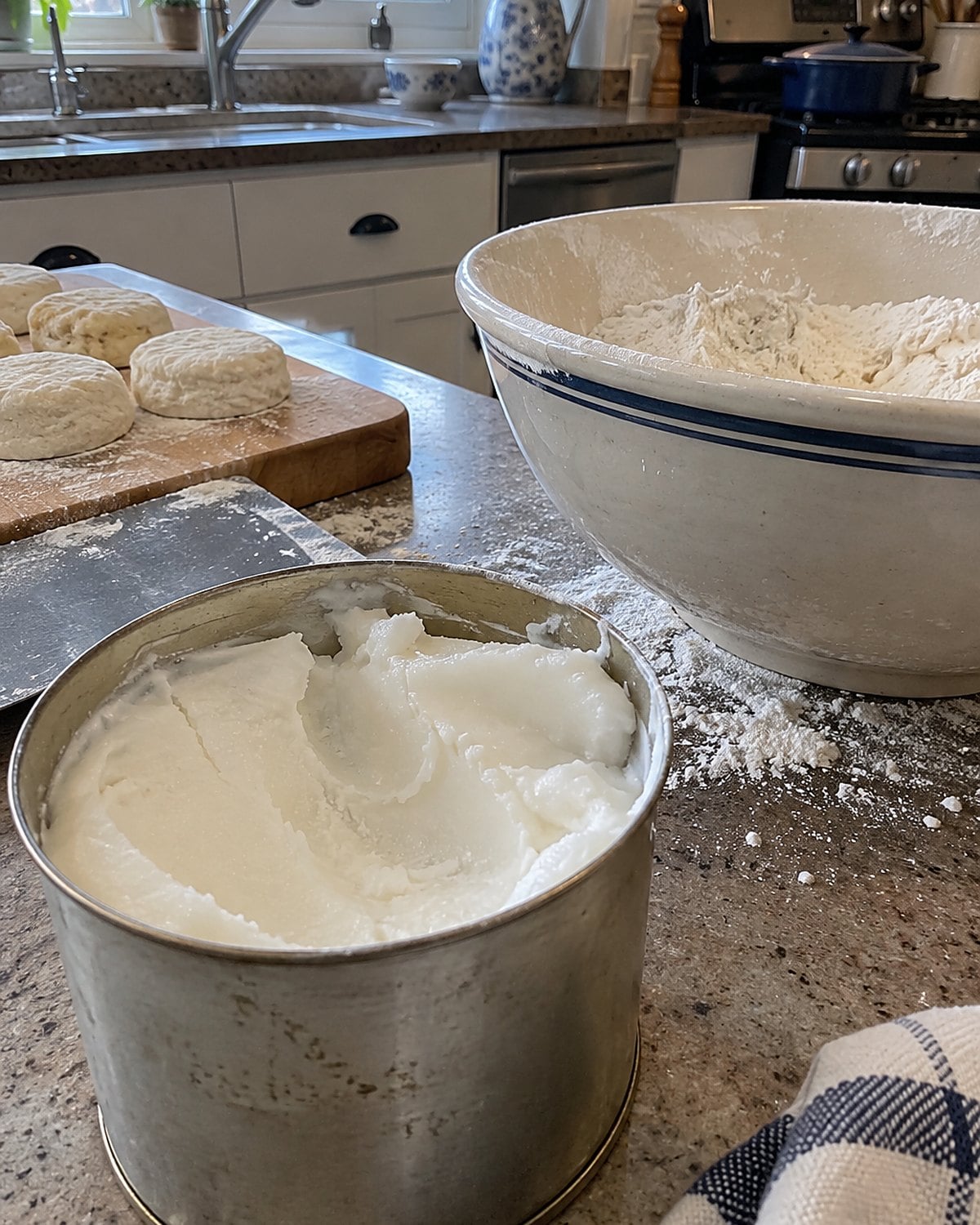 An open tin of lard beside a flour-dusted bowl on a worn kitchen counter.